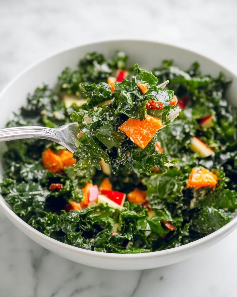 A white bowl filled with a leafy kale salad showing dark green, curly kale leaves as the main layer. Mixed throughout the kale are bright orange chunks of roasted squash or sweet potato and small pieces of red apple, adding a fresh pop of color. The texture looks a bit creamy, suggesting a light dressing coating the leaves and vegetables. A silver fork is lifting a generous bite from the bowl, showing a close-up of the green kale with orange and red bits on top. The bowl sits on a white marbled surface, making the colors stand out clearly. photo taken with an iphone --ar 4:5 --v 7