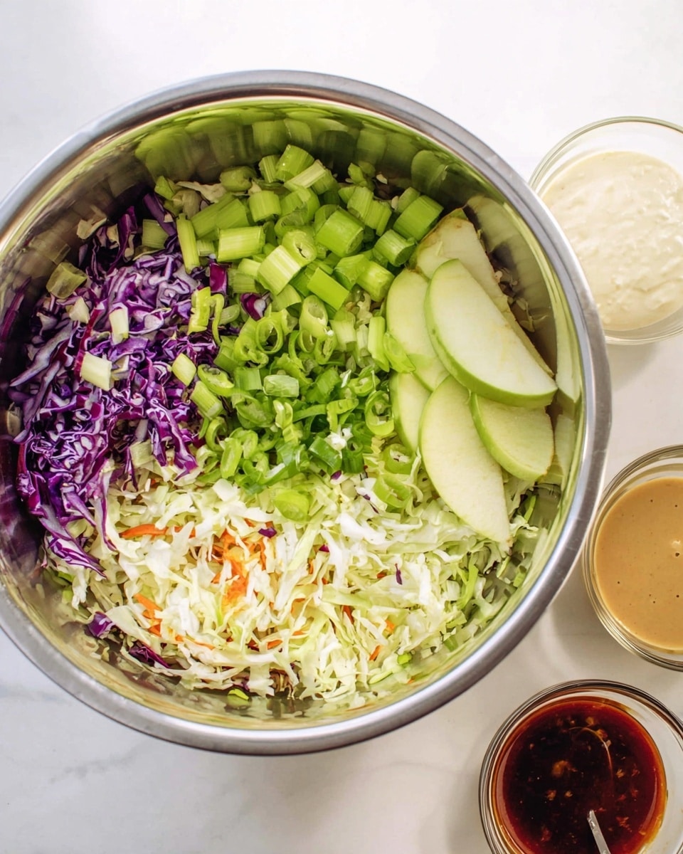 A large silver mixing bowl on a white marbled surface holds a colorful layered salad. The bottom layer is a mix of shredded white and purple cabbage with small bits of orange carrot. On top of this base, there are piles of chopped light green celery sticks on the left, finely sliced bright green scallions in the middle, and thin slices of green apple on the right side. Next to the bowl, there are two small glass bowls containing creamy white and dark reddish-brown sauces. The scene is bright and fresh, with all ingredients clearly visible. Photo taken with an iphone --ar 4:5 --v 7