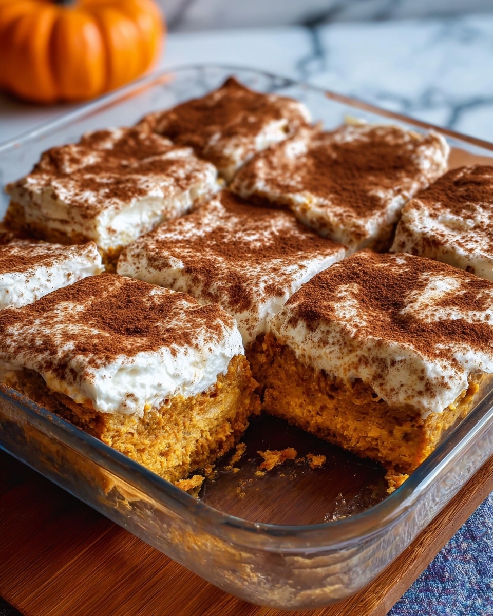 A square piece of yellow baked dessert with a slightly browned top sits in the middle of a white plate with brown speckles. On top of the dessert is a dollop of white whipped cream sprinkled with a light dusting of cinnamon. A gold fork rests on the right side of the plate, partially under the dessert. The plate is placed on a white marbled surface with cinnamon sticks in the foreground and a blurred pumpkin and white pottery in the background. Photo taken with an iphone --ar 4:5 --v 7