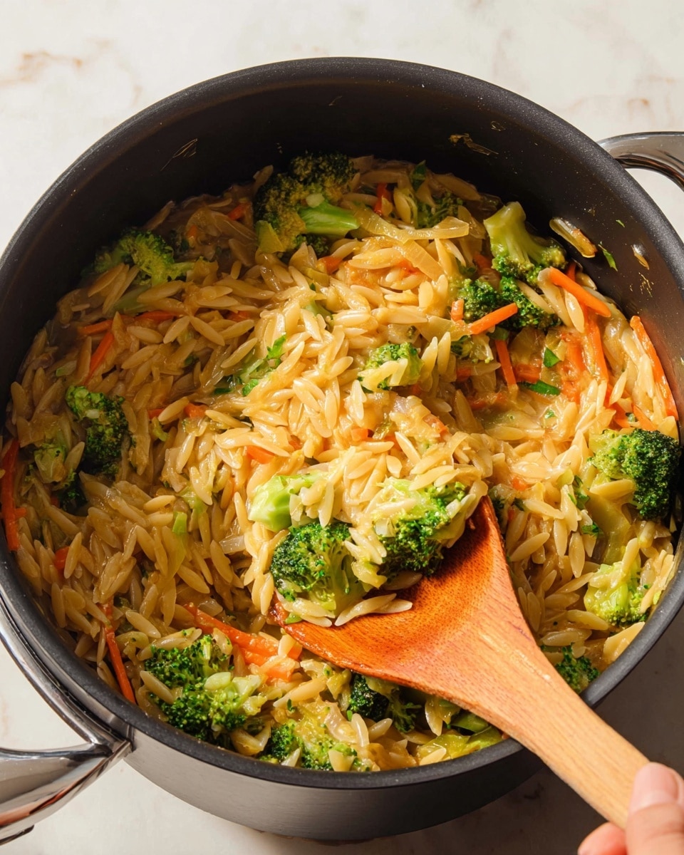 The image shows a black cooking pot filled with a mix of small, oval-shaped pasta, bright green broccoli florets, thin orange carrot strips, and light brown onion pieces, all stirred together with a wooden spatula. The pasta looks soft and shiny, mixed evenly with the fresh vegetables that add a pop of color and texture. The pot is placed on a white marbled surface, and a woman's hand is holding the wooden spatula, lifting a portion of the pasta and vegetables. The overall scene looks warm and inviting, with natural lighting highlighting the steam and moisture of the dish. photo taken with an iphone --ar 4:5 --v 7