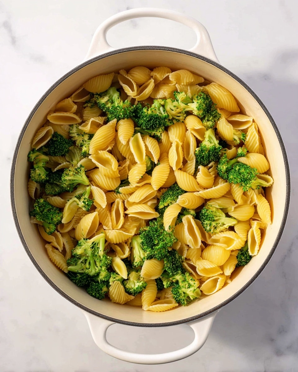 A white pot filled with two main layers: the bottom layer is yellow, ridged shell pasta that fills most of the pot, and mixed evenly throughout are bright green broccoli florets with a textured surface and short stems. The pot has handles on each side, and it sits on a white marbled surface. The lighting is bright and natural, showing the details and colors clearly. photo taken with an iphone --ar 4:5 --v 7