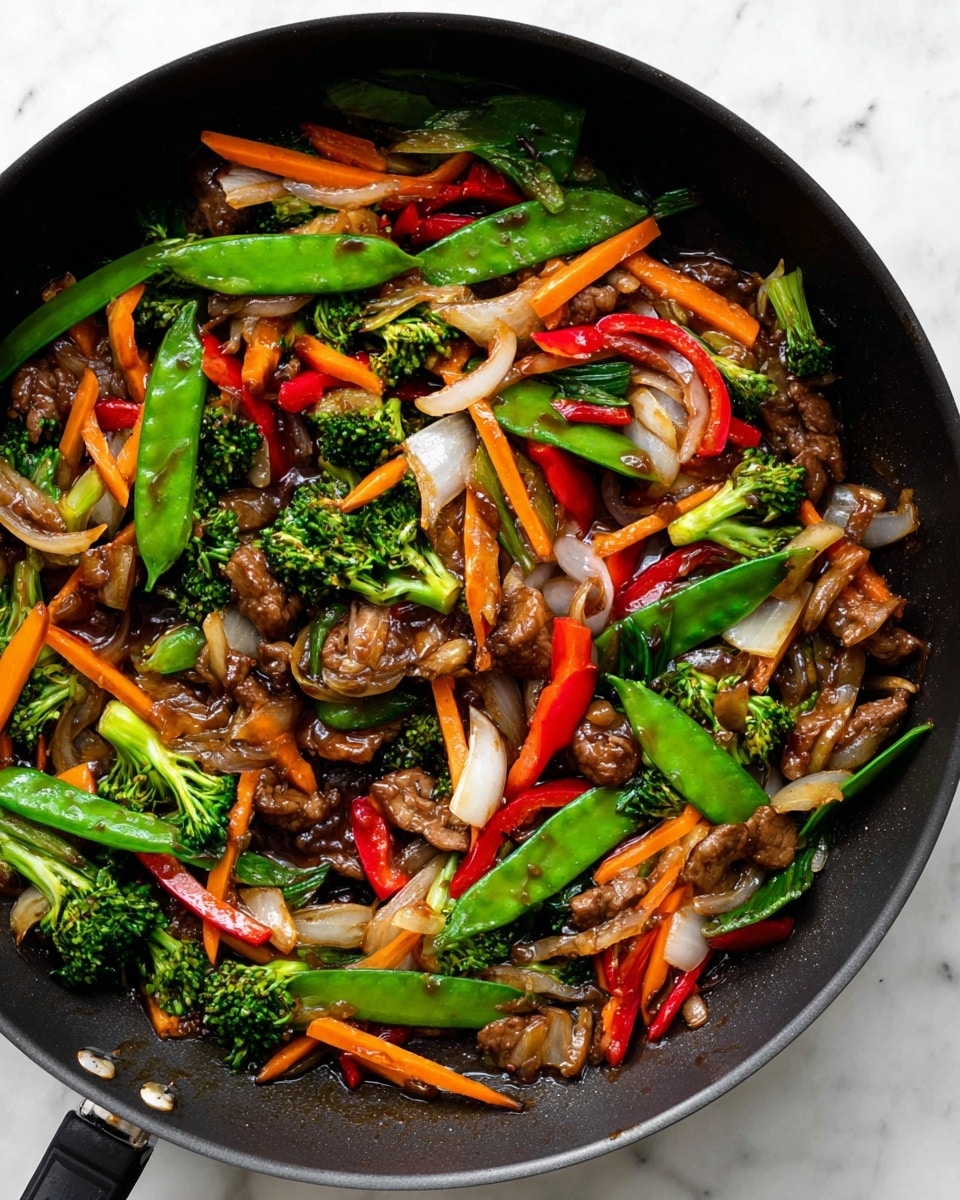 The image shows a black frying pan filled with colorful stir-fry. The dish has several layers including bright green snap peas and broccoli florets scattered on top, thin orange carrot sticks, red bell pepper strips, and chopped white onions with some slightly browned edges. There are also small pieces of cooked brown meat and light brown mushrooms mixed evenly throughout. Everything is coated in a glossy, dark sauce that adds shine to the vegetables and meat. The pan is placed on a white marbled surface, highlighting the vibrant colors of the stir-fry. Photo taken with an iphone --ar 4:5 --v 7