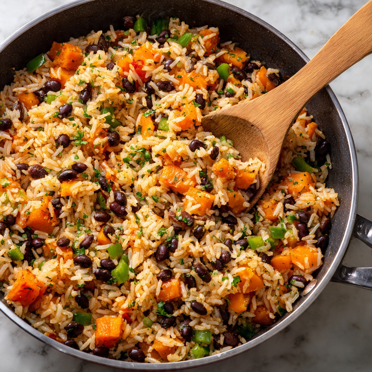 A close-up view of a pan filled with a colorful mix of cooked white rice, black beans, and diced orange sweet potatoes, with green bell pepper pieces scattered throughout. The mixture shows a soft texture with a hint of herbs or seasoning. A wooden spoon scoops some of the rice and vegetable mix from the pan. The pan's edge is visible, sitting on a white marbled surface. photo taken with an iphone --ar 4:5 --v 7