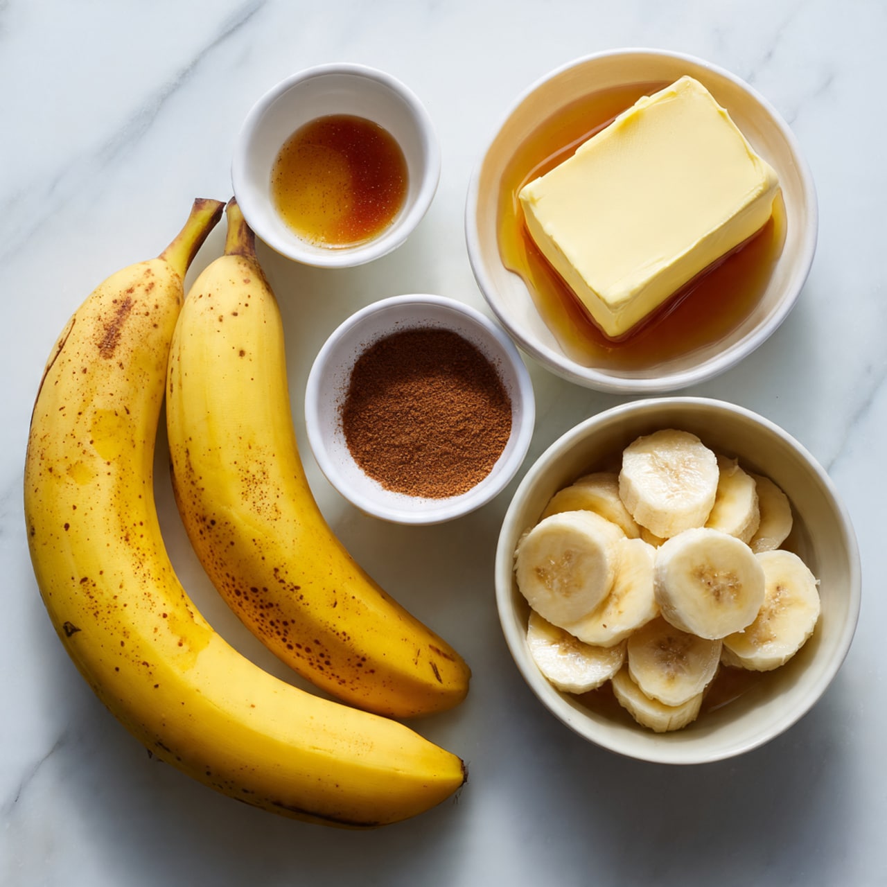 The image shows two whole yellow bananas with small brown spots on a white marbled surface. Next to them are four white bowls: the top one contains a block of butter with some melted butter around it, the middle one has a pile of brown cinnamon powder, the bottom one holds a small amount of honey or syrup, and the larger bowl on the right is filled with thick banana slices. The bowls and bananas are arranged in a loose square shape. The lighting is bright and natural, giving a clean and fresh look. Photo taken with an iphone --ar 4:5 --v 7