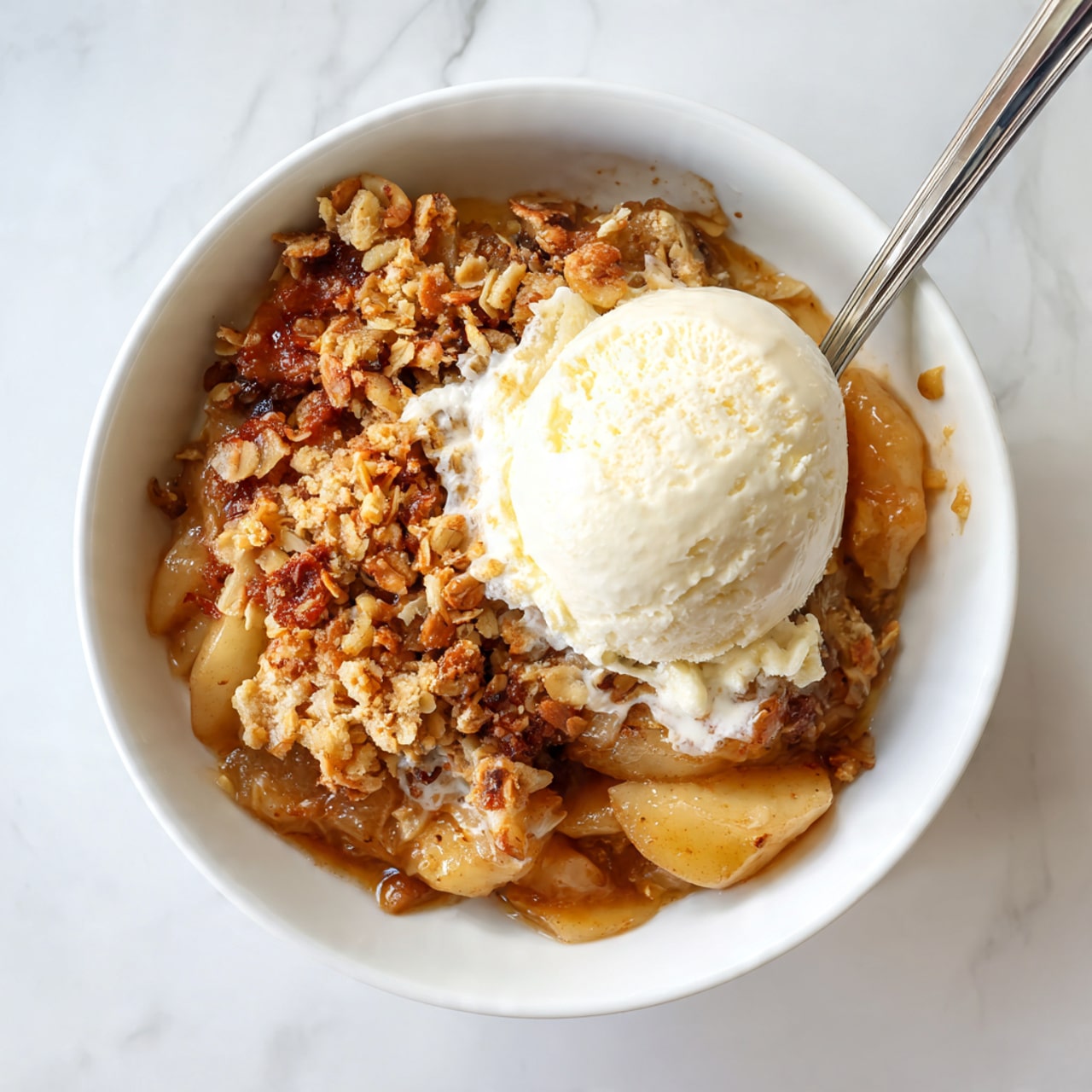 A white bowl holds a dessert with three main layers: the bottom layer is warm, soft baked apple pieces mixed with a sticky cinnamon sauce showing a brownish color; the middle layer consists of crunchy, golden-brown oat and nut crumble scattered on top of the apples; the top layer is a single, smooth, creamy scoop of pale vanilla ice cream sitting in the center, slightly melting at the base where it meets the warm crumble and apples. The bowl is placed on a white marbled textured surface. Photo taken with an iphone --ar 4:5 --v 7