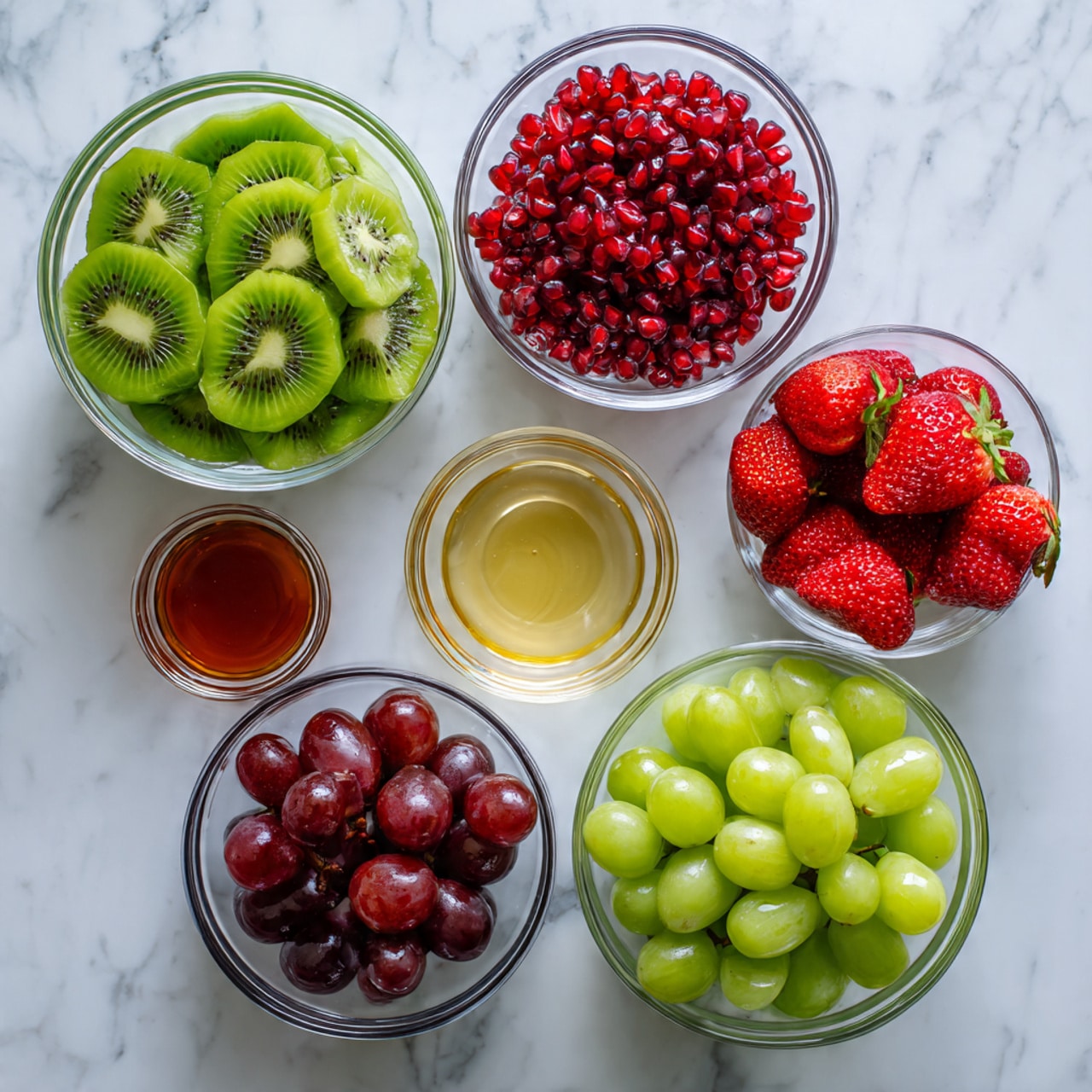 There are six clear glass bowls arranged on a white marbled surface. The top left bowl is filled with green kiwi slices, each slice showing its light green flesh and tiny black seeds in a circular pattern. To the right of it is a small bowl with bright red pomegranate seeds. Below the kiwi bowl is a larger bowl filled with dark red grapes with smooth skins. Next to it on the right is a bowl of fresh red strawberries with green leafy tops visible. Below the grapes is a bowl of light green grapes, round and shiny. To the left of the green grapes is a small bowl of golden honey, and to the right of the green grapes is a small bowl of clear lemon juice. The bowls are neatly spaced out, and the colors of the fruits stand out against the clean white marbled background. photo taken with an iphone --ar 4:5 --v 7