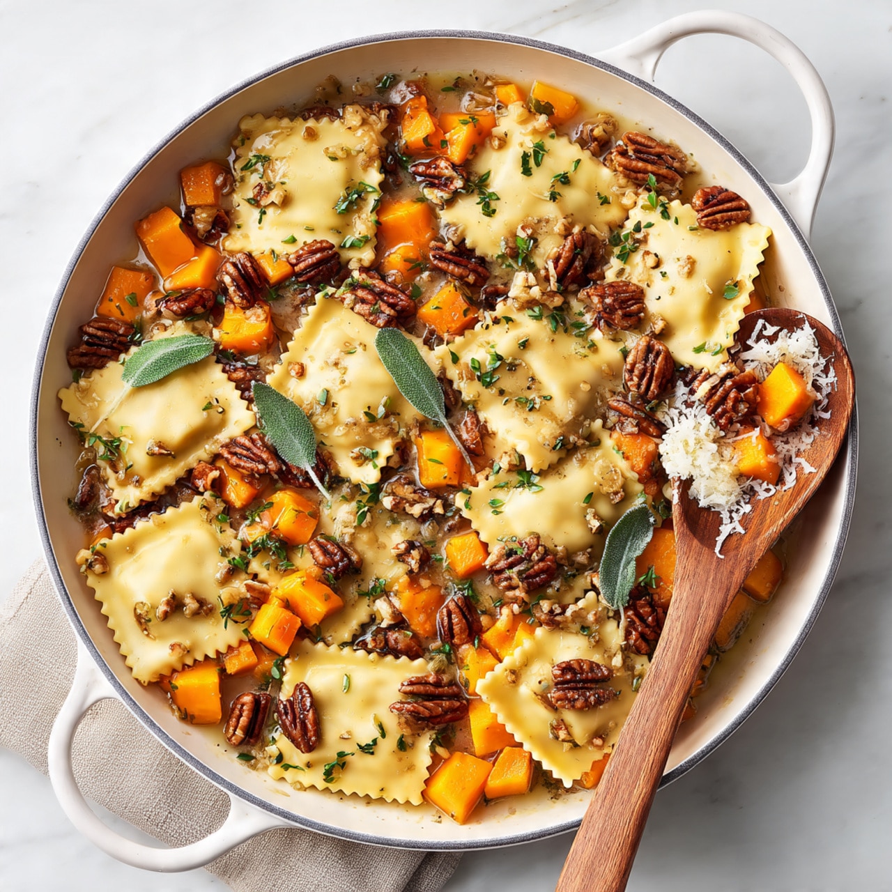 The dish is served in a white pan placed on a white marbled surface. It contains a layer of square ravioli with a light yellow color, some edges showing a slightly ruffled texture. Mixed with the ravioli are small cubes of bright orange butternut squash spread evenly throughout. On top of the pasta, there is a sprinkling of chopped pecans, dark brown with rough edges, and some sage leaves that add a touch of dark green. There is also a small mound of white grated cheese sitting on one side. A wooden spoon rests on the right side of the pan, scooping some of the ravioli and squash. Photo taken with an iphone --ar 4:5 --v 7