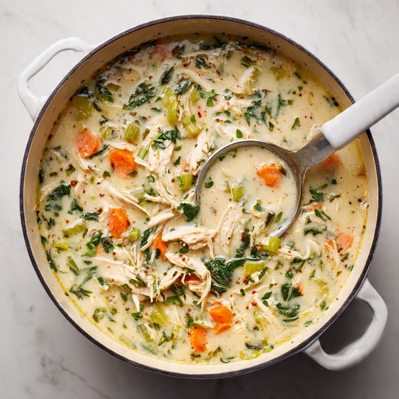 The image shows a white pot filled with creamy chicken soup, containing layers of shredded white chicken, bright orange carrot slices, light green celery pieces, and dark green leafy herbs spread evenly throughout the creamy soup base. A silver ladle with a white handle dips into the soup from the top right side. The pot is set on a white marbled surface. photo taken with an iphone --ar 4:5 --v 7