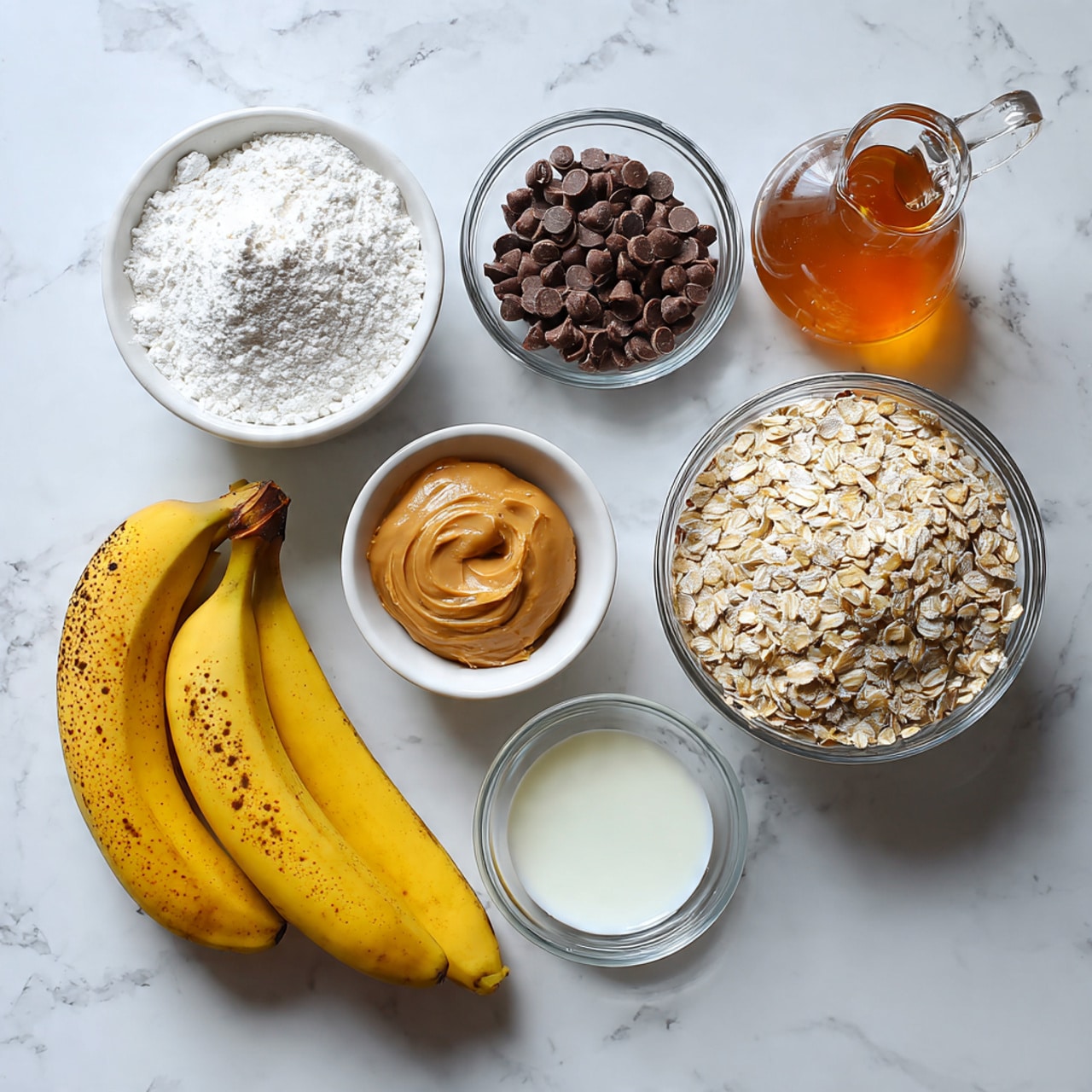 The image shows several baking ingredients spread on a white marbled surface. Starting from the top left, there is a small metal spoon filled with white baking powder, next to a clear glass bowl filled with small dark brown chocolate chips. To the right, a clear glass jug holds amber-colored maple syrup. Below these, two yellow bananas with small brown spots rest side by side. On the left, a single brown egg is placed near a white bowl filled with creamy peanut butter in the center of the image. Beneath that, a small clear bowl contains solid white oil. At the bottom right corner, a large clear bowl is filled with pale beige rolled oats. Each ingredient is clearly visible with distinct textures and colors, all placed neatly apart from each other on the smooth white marbled surface. photo taken with an iphone --ar 4:5 --v 7