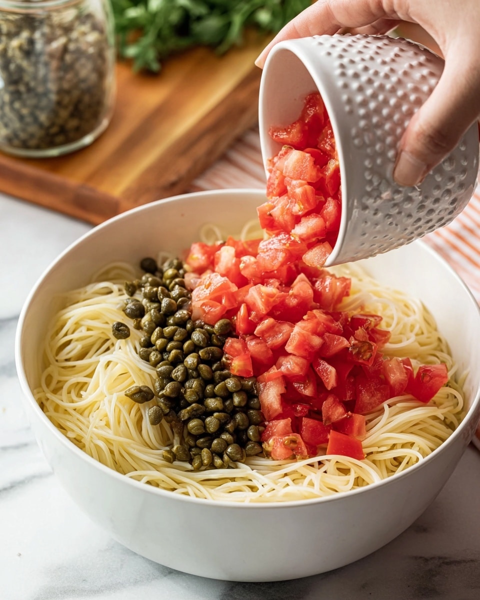 A white bowl filled with three layers is shown: the bottom layer is thin cooked spaghetti with a pale yellow color, the middle layer is dark green capers piled on one side, and the top layer is bright red diced tomatoes being poured from a small white bowl with a dotted texture by a woman's hand. The bowl sits on a white marbled surface, with a blurred wooden board and green herbs in the background. A glass jar with more capers is partially visible in the corner. Photo taken with an iphone --ar 4:5 --v 7