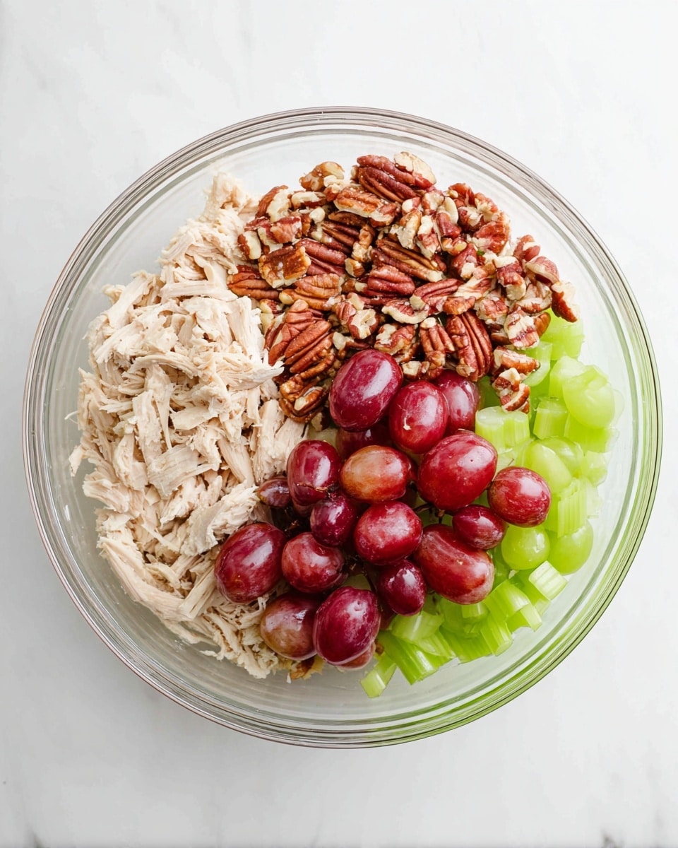 A clear glass bowl sits on a white marbled surface, holding four separate layers of ingredients. One layer consists of pale shredded chicken placed on the left side. Next to it on the right is a bright green layer of sliced celery, showing smooth, fresh texture. Above the celery is a pile of chopped light brown pecans with rough edges, and the final layer at the top is made of halved red grapes showing their smooth, shiny skin and pale interiors. The layers stay separate with clear color contrasts, all inside the transparent bowl photo taken with an iphone --ar 4:5 --v 7
