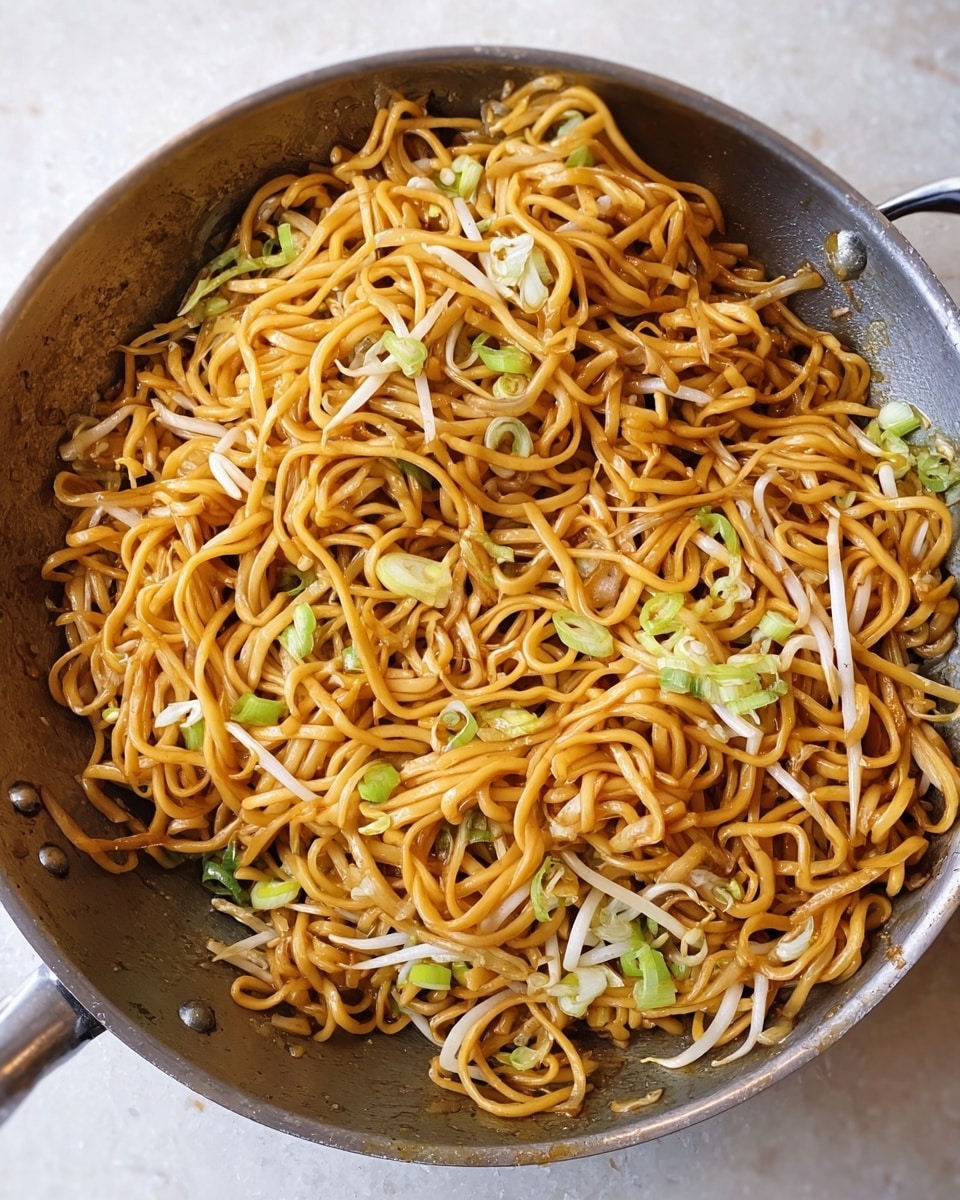 This image shows a close-up of a round metal pan filled with stir-fried noodles. The noodles are thick and yellowish-orange, mixed with scattered light green sliced spring onions and white bean sprouts, adding a fresh texture. The noodles are shiny and lightly coated with a sauce, giving some strands a glazed look. The pan rests on a white marbled surface, enhancing the colors of the food inside. photo taken with an iphone --ar 4:5 --v 7