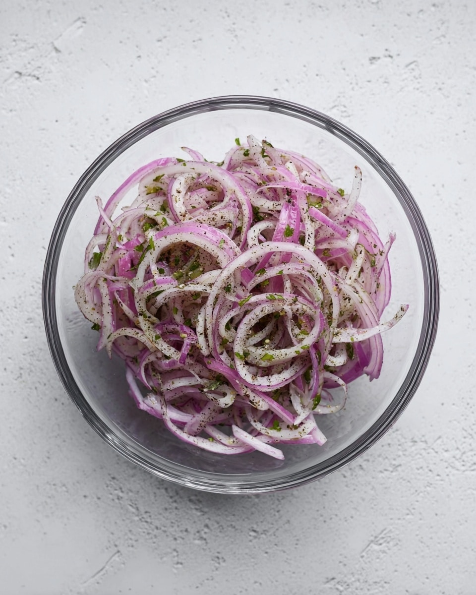 A clear glass bowl sits on a white marbled surface filled with thinly sliced red onions that are pale purple with white stripes. The onions are mixed with small pieces of green herbs and specks of black seasoning spread evenly throughout. The texture looks light and fresh, with the onion slices curved and layered loosely on top of each other. The bowl is round and transparent, showing all the contents clearly from above. photo taken with an iphone --ar 4:5 --v 7