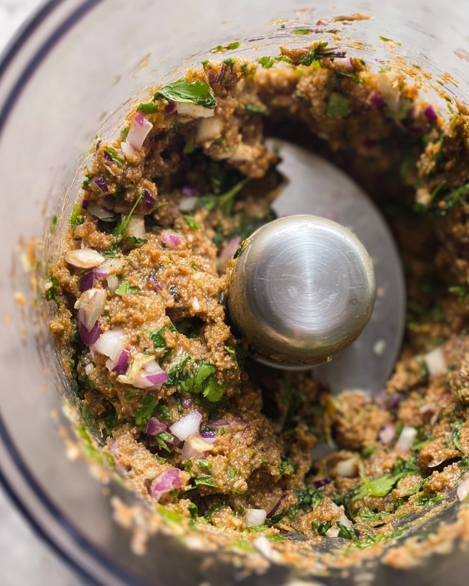 The image shows a close-up view inside a blender jar filled with a coarse mixture, featuring multiple layers of finely chopped ingredients. The mixture contains green leafy bits, likely cilantro or parsley, dispersed evenly throughout. There are small pieces of white onion and purple-red bits, which appear to be red onion, creating a colorful texture. The overall color varies from light tan to dark brown, with a moist and chunky consistency. The metal blender blades are at the center, partially submerged under the mixture. The jar is transparent plastic with a white marbled surface background barely visible outside. photo taken with an iphone --ar 4:5 --v 7