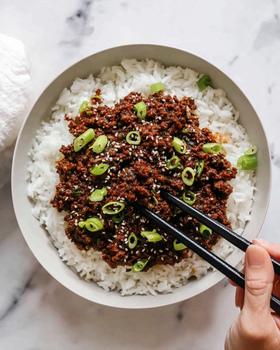 A bowl filled with two main layers is shown. The bottom layer is white fluffy rice with a slightly sticky texture, spreading evenly across the bowl. On top, there is a thick layer of dark brown minced meat sauce with small pieces of finely cooked vegetables, looking moist and rich. The minced meat is garnished with small slices of fresh green spring onions scattered around and some white sesame seeds sprinkled on top. A woman's hand holding black chopsticks is reaching toward the center of the bowl, as if about to pick up some food. The bowl is white and placed on a white marbled surface. photo taken with an iphone --ar 4:5 --v 7