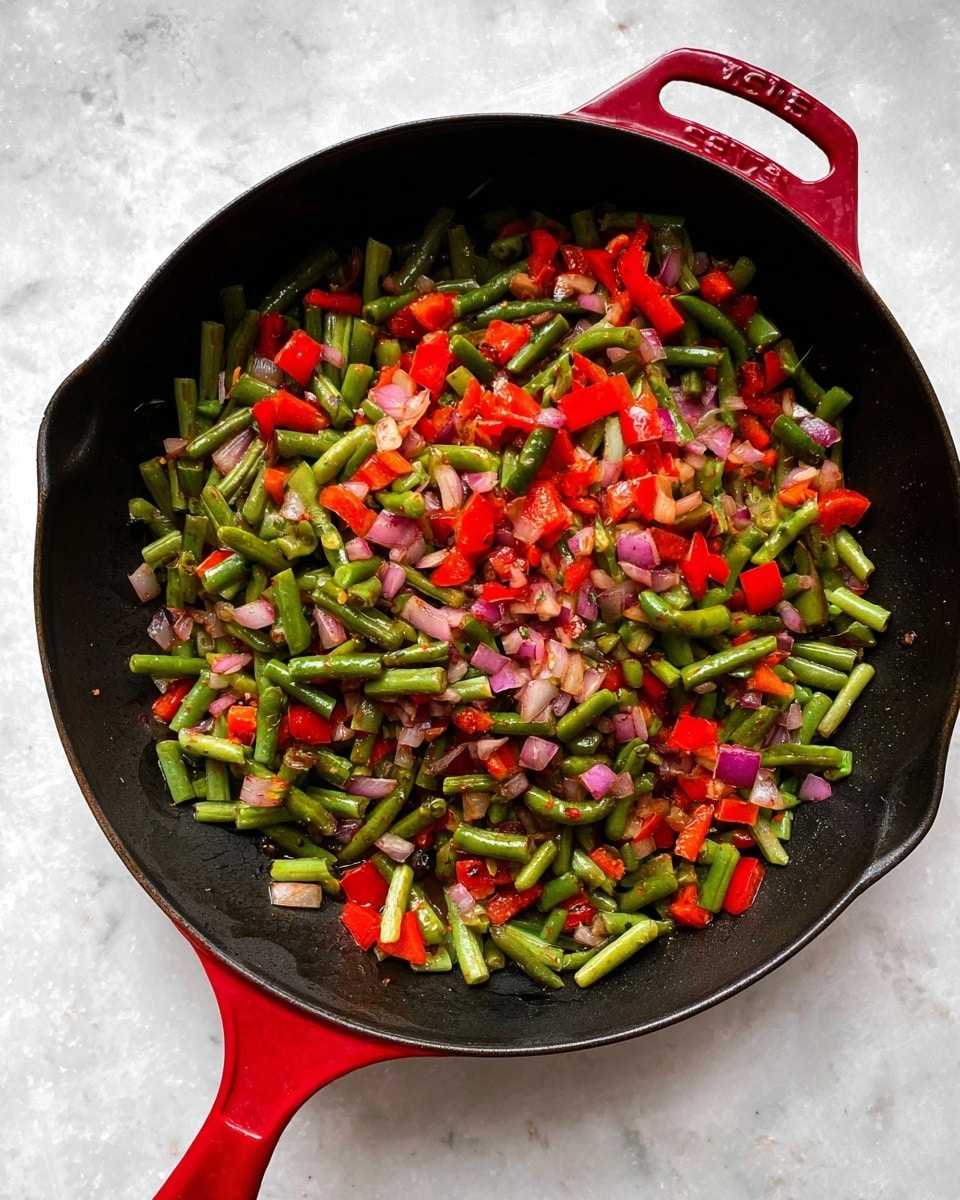 A black cooking pan with a red handle filled with three layers of cooked vegetables: a mix of chopped green beans, red bell peppers, and diced red onions. The vegetables are mixed well with a slightly glossy texture, showing light seasoning and a soft, cooked look. The pan rests on a white marbled surface. Photo taken with an iphone --ar 4:5 --v 7