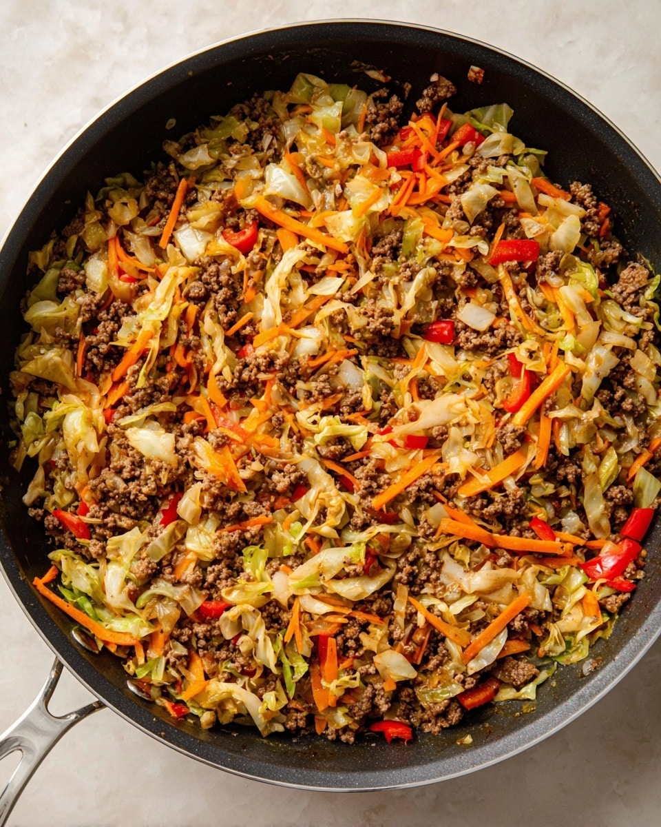The image shows a large black frying pan filled with a cooked mix of ground meat, shredded cabbage, thin orange carrot strips, and small pieces of red bell pepper. The mixture is evenly spread in the pan with a mix of brown, white, orange, and red colors creating a textured and hearty surface. The pan sits on a white marbled surface, and no other objects are visible. The focus is on the colorful cooked ingredients inside the pan, giving a warm and home-cooked feel. photo taken with an iphone --ar 4:5 --v 7