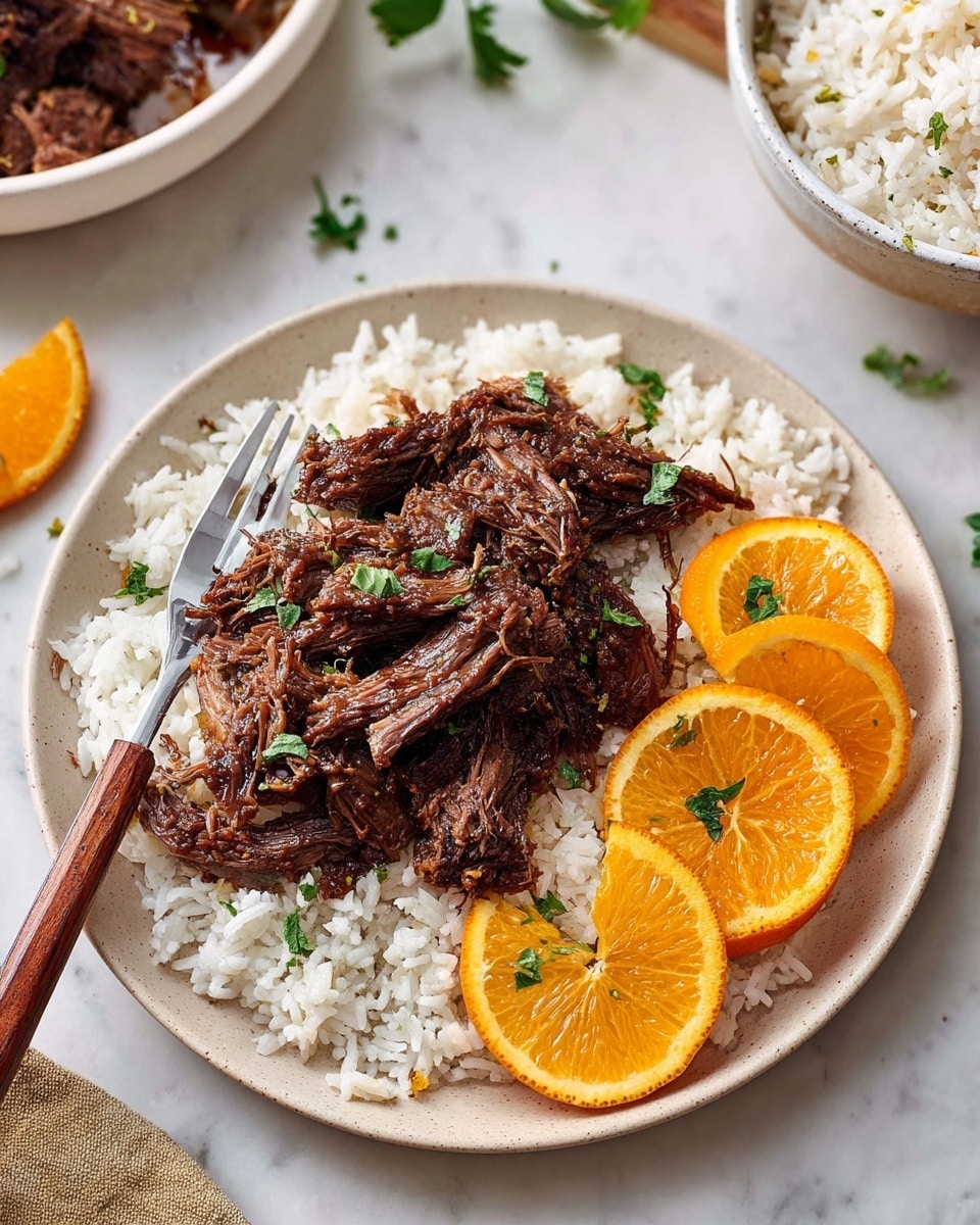 A white plate sits on a white marbled surface, filled with two main layers: the bottom layer is fluffy white rice with a soft texture, and on top is a generous portion of dark brown shredded meat with a slightly glossy finish indicating sauce. On one side of the plate, there are three bright orange slices arranged overlapping, each garnished with small sprigs of green herbs, matching the scattered herbs on the meat. A fork with a wooden handle rests on the left edge of the plate. In the upper right corner, part of a white bowl filled with white rice is visible. Photo taken with an iphone --ar 4:5 --v 7
