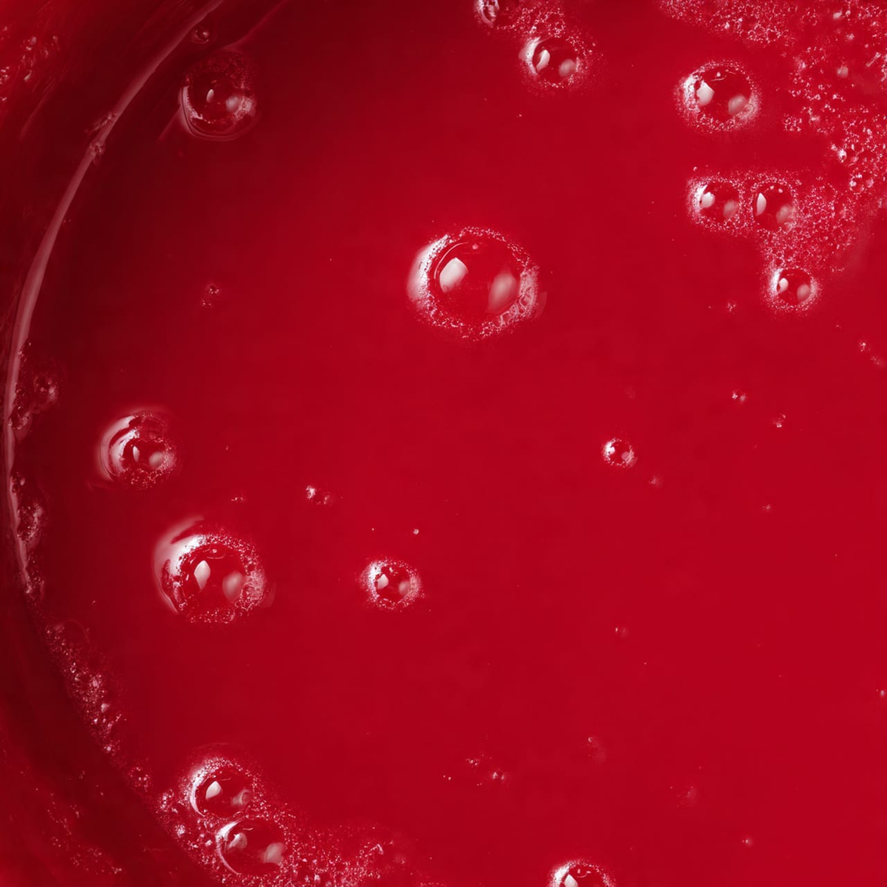 The image shows a close-up of a single layer of bright, deep red sauce or batter with a smooth and shiny texture, filling a round white bowl. The surface has small bubbles and slight unevenness in texture, giving it a fresh and liquid look. The edges of the bowl show some streaks of the red mixture, emphasizing its thickness. The background is a white marbled texture, making the vibrant red color stand out clearly. photo taken with an iphone --ar 4:5 --v 7