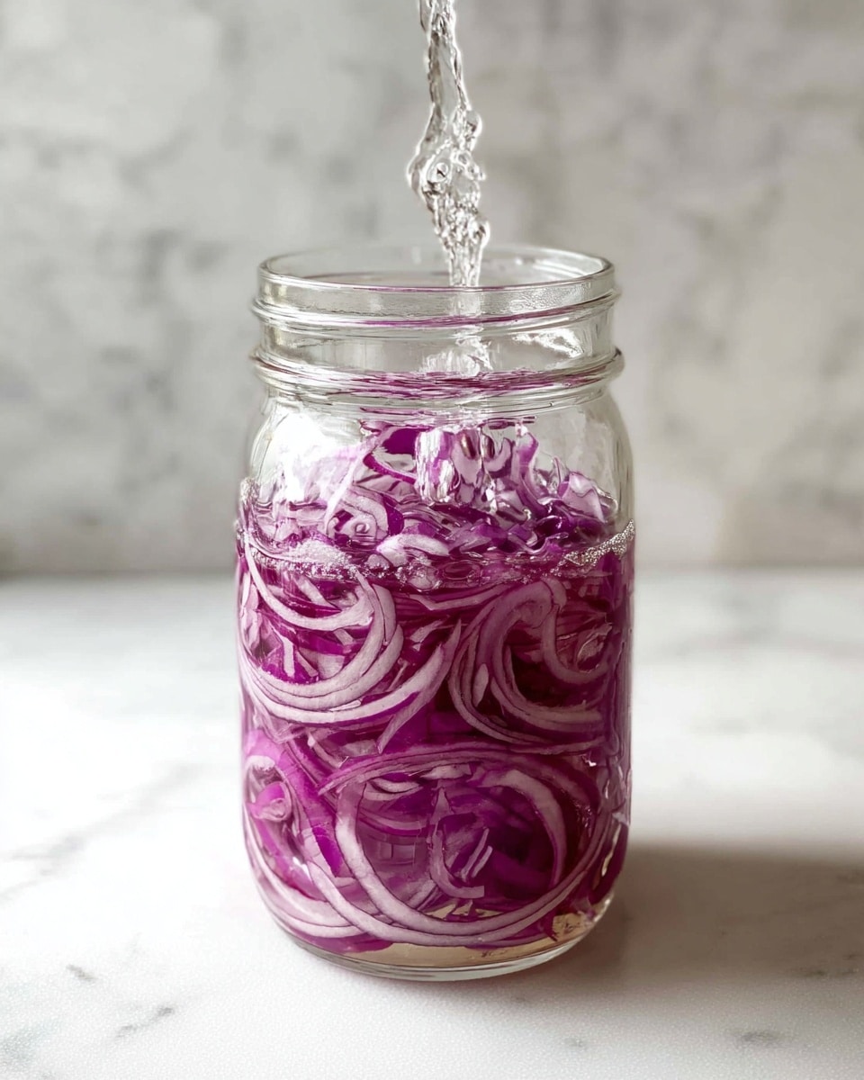 A clear glass jar filled with thin slices of purple-red onions. The onions are tightly layered inside the jar, showing rings and curly shapes all around. Clear liquid is being poured into the jar from the top, creating bubbles and small splashes visible among the onions. The jar sits on a white marbled surface with a soft, blurred white marbled background behind it. The light softly shines on the jar, highlighting the textures of the onions and the glass. photo taken with an iphone --ar 4:5 --v 7