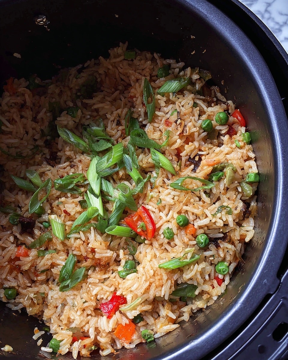 A close-up of cooked rice mixed with small pieces of green peas, red bell pepper, chopped green onions, and other vegetables, all inside a dark air fryer basket. The rice is slightly browned and mixed with green scallion slices scattered on top. The background has a white marbled texture. photo taken with an iphone --ar 4:5 --v 7