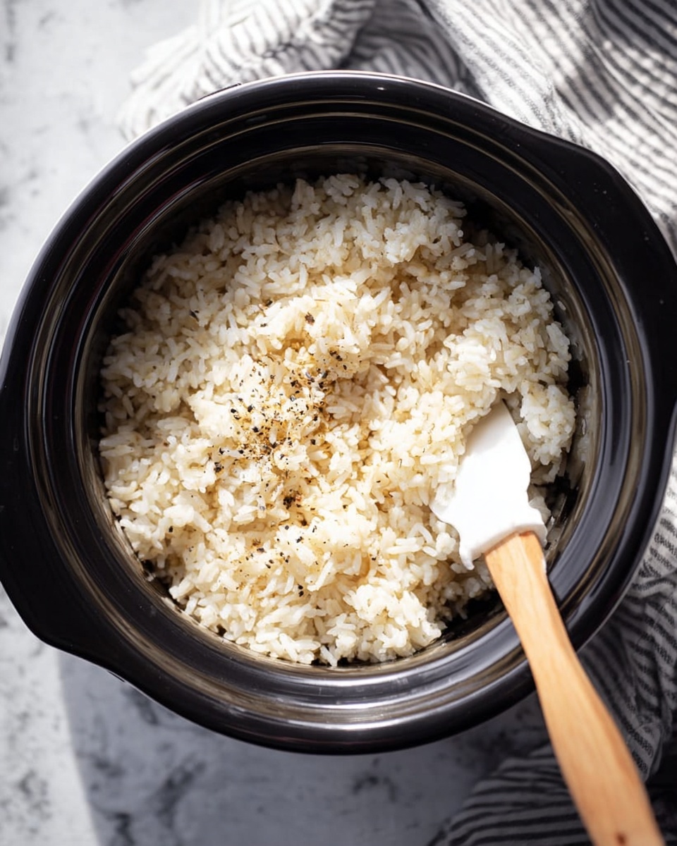 A black round rice cooker filled with cooked white rice mixed with light brown seasoning grains, showing a slightly fluffy texture. A white rice paddle with some black pepper is resting inside on the right side, partially buried in the rice. The rice cooker is placed on a white marbled surface with a striped cloth partially visible at the top right corner. The lighting is soft and natural, highlighting the textures of the rice. photo taken with an iphone --ar 4:5 --v 7