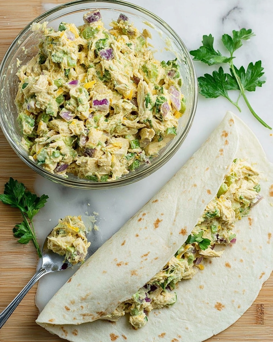 A clear glass bowl filled with a chunky mixture of shredded light yellow and green chicken salad with visible pieces of purple onion and green herbs, sitting on a white marbled textured surface. Next to the bowl, a white round tortilla is partially rolled with the same chunky chicken salad spread unevenly across it, showing bits of purple onion, green herbs, and orange cheese inside the wrap. A metal spoon with a bit of the chicken salad on it rests nearby. Fresh green parsley leaves lay beside the tortilla on the surface. Photo taken with an iphone --ar 4:5 --v 7