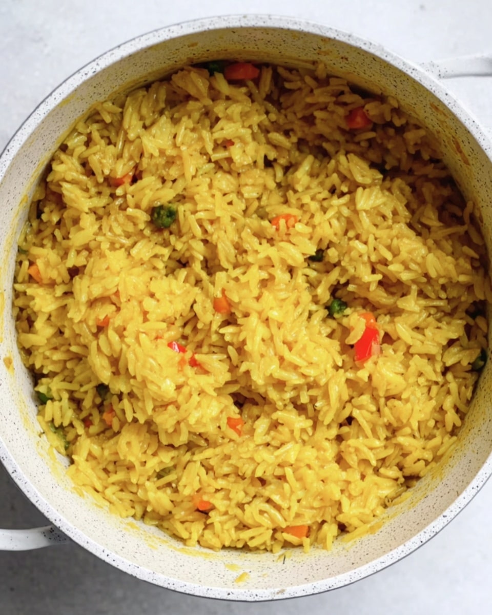 A close-up top view of a single layer of cooked yellow rice with small bits of vegetables mixed in, filling a white speckled pot, showing a soft and slightly moist texture. The pot is placed on a white marbled surface. photo taken with an iphone --ar 4:5 --v 7