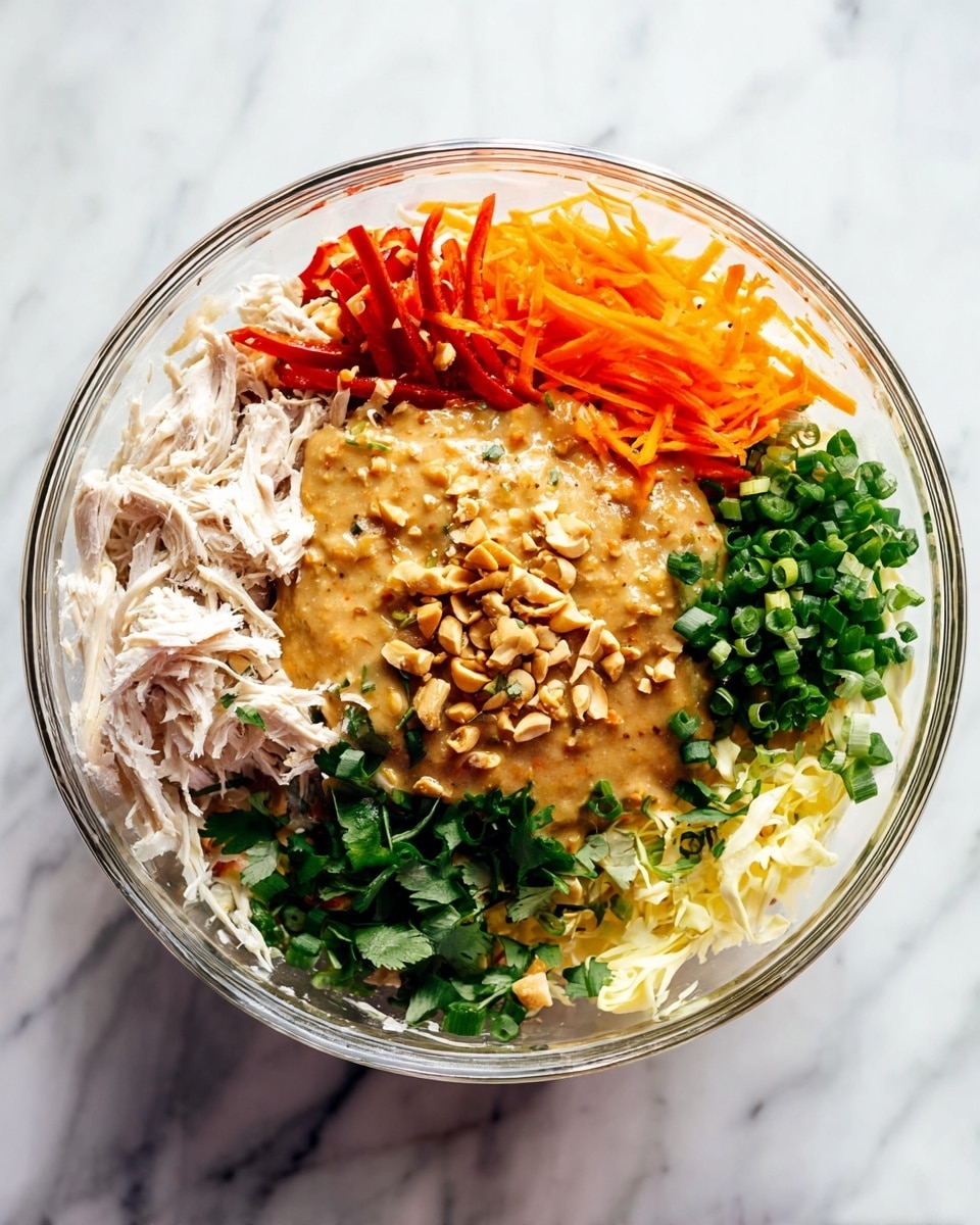 A clear glass bowl sits on a white marbled surface filled with several colorful layers of ingredients. Starting from the left side, there is a pile of shredded white meat on the edge, next to some thin slices of red chili. At the top, there is a small pile of bright orange shredded carrots. The middle section holds a thick, light brown sauce with bits of chopped nuts on top. Surrounding the sauce are fresh green herbs including chopped scallions and cilantro. At the bottom, there is a layer of pale yellow shredded vegetable. All the ingredients are arranged separately in sections inside the bowl, ready to be mixed. Photo taken with an iphone --ar 4:5 --v 7