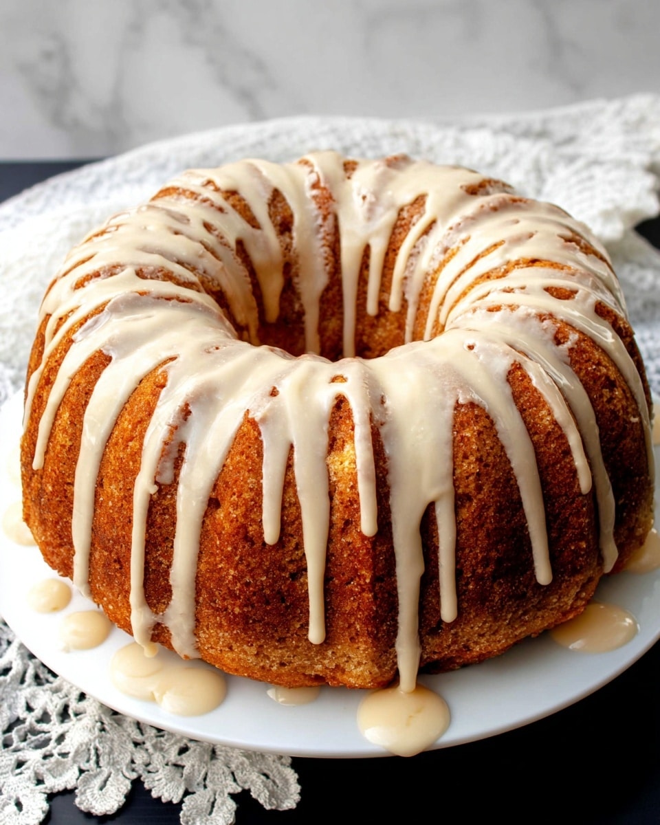 A round bundt cake with one thick layer showing a light brown baked texture, sitting on a white plate. The top of the cake is covered with thick off-white glaze dripping down the sides evenly in long lines. Some drops of glaze are on the plate around the cake. The background is a white marbled surface with a folded white lace-edged cloth near the plate. Photo taken with an iphone --ar 4:5 --v 7
