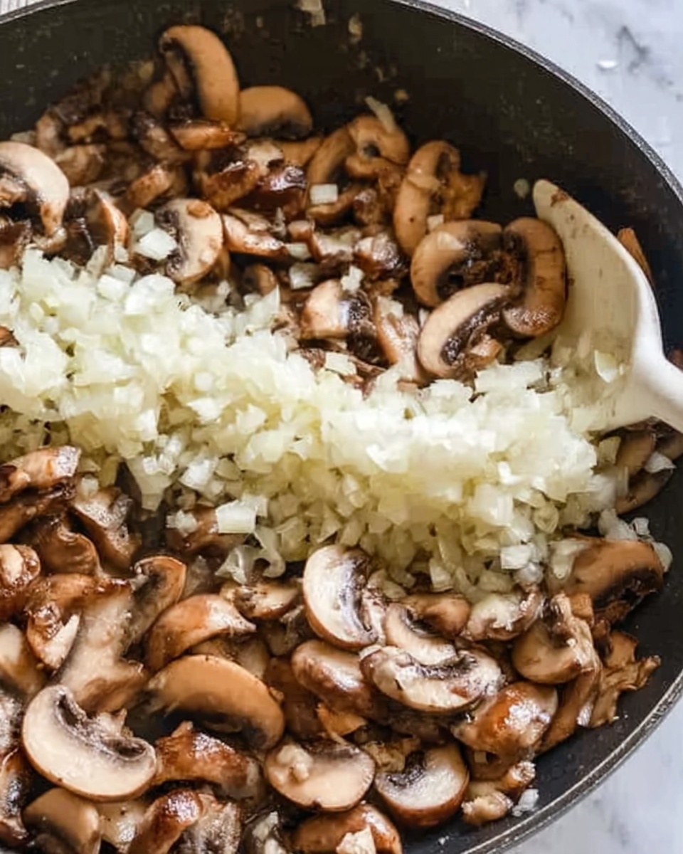The image shows a close-up of a sauté pan filled with cooked sliced mushrooms with a golden-brown color around the edges, covering most of the pan's surface. In the middle of the pan, a line of finely chopped white onions is spread out, contrasting with the darker mushrooms. A white spatula is partially visible, resting on the edge of the onions and mushrooms. The texture of the mushrooms looks soft and slightly wrinkled, while the onions appear fresh and slightly translucent. The background is a white marbled surface. Photo taken with an iphone --ar 4:5 --v 7