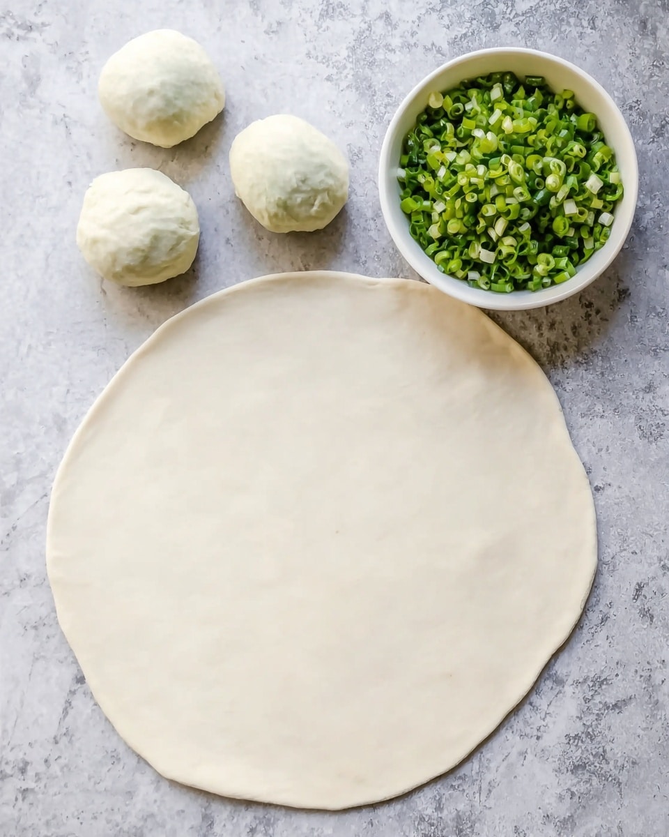 A large, thin, round dough sheet lies flat on a white marbled surface. Above it, there are three dough balls placed close together. To the upper right, there is a white bowl filled with chopped green onions, showing fresh green colors and a textured look. The colors in the image are mainly white and green, with the dough looking smooth and slightly translucent, while the chopped green onions add a vibrant contrast. Photo taken with an iphone --ar 4:5 --v 7