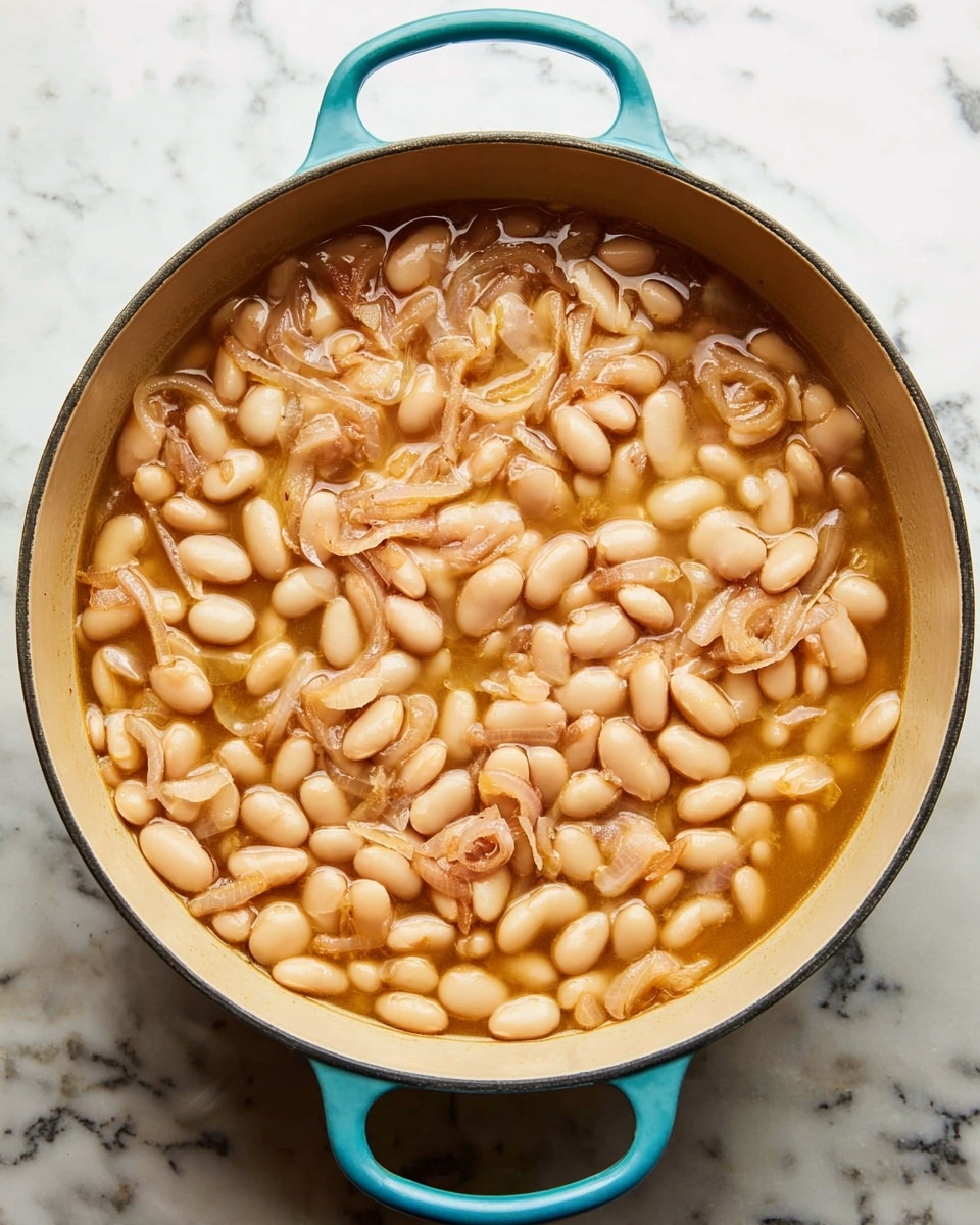 A top view of a large turquoise pot filled with a thick soup of white beans in light brown broth, with thin slices of cooked shallots scattered evenly throughout. The beans are soft and plump, covering the entire inner surface of the cream-colored pot, which sits on a white marbled surface. The broth is slightly glossy, surrounding the beans and shallots, giving a warm and comforting appearance. photo taken with an iphone --ar 4:5 --v 7