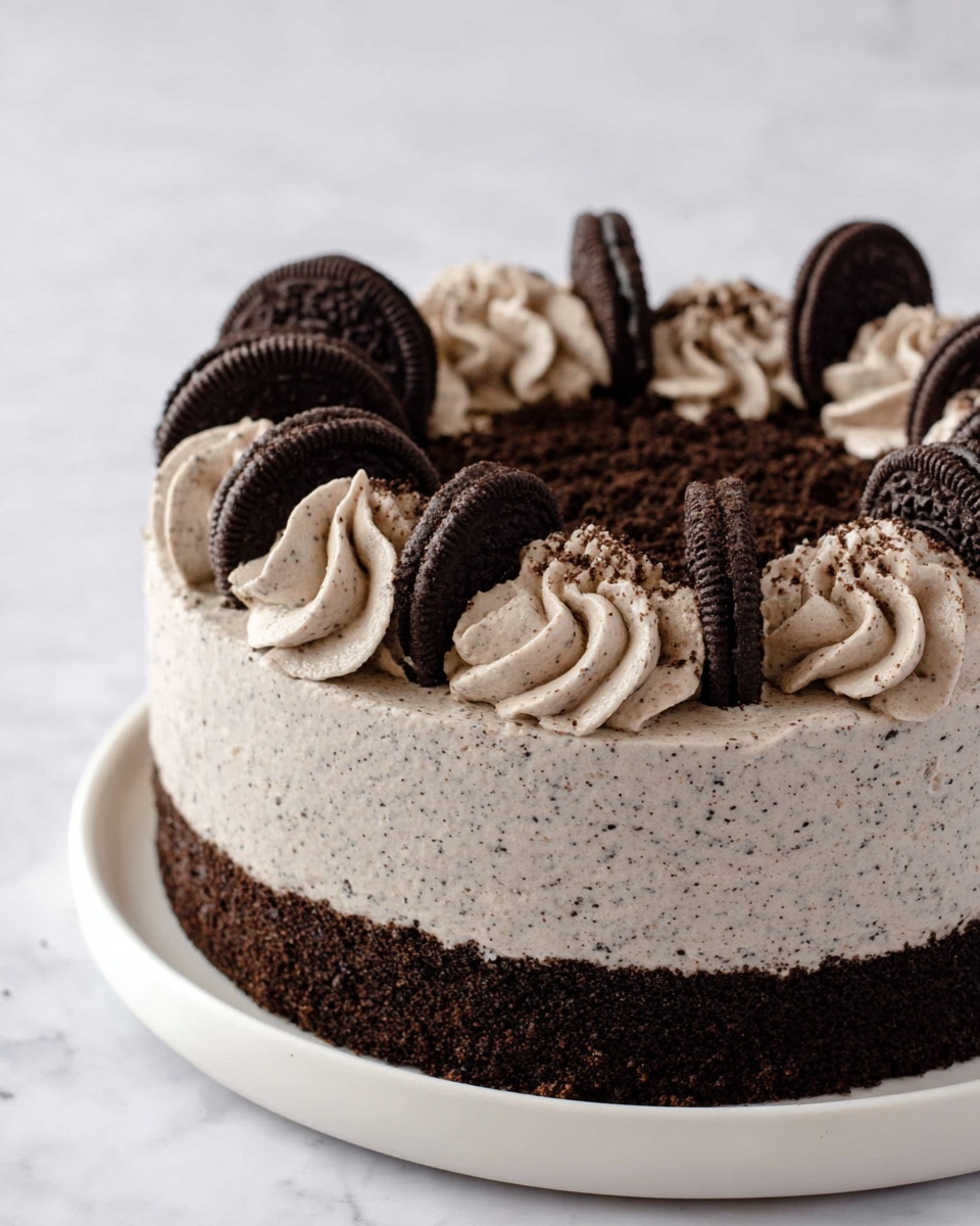 A round cake with two visible layers is shown on a white plate, placed on a white marbled surface. The bottom layer is dark brown and crumbly, while the top layer is light gray with tiny dark specks throughout, smooth and creamy in texture. Around the top edge of the cake, there are evenly spaced swirls of light gray cream with dark specks, and each swirl holds a half of a dark chocolate cookie standing upright. The very top center of the cake is covered with a thin layer of finely crushed dark crumbs in a circle. The photo taken with an iphone --ar 4:5 --v 7