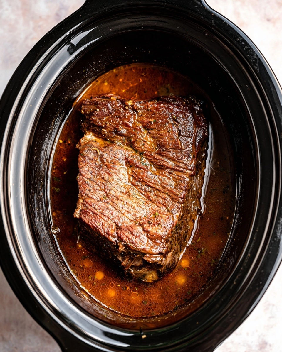 A large piece of cooked beef with a dark brown crust sits in a black slow cooker filled halfway with glossy, rich brown broth. The beef has visible grilled texture and slight fat patches on top, resting in a thick layer of liquid that covers the bottom but leaves the beef mostly exposed. The slow cooker glossy black pot with its smooth inner surface contrasts with the cooked beef, and the background shows a white marbled texture. Photo taken with an iphone --ar 4:5 --v 7