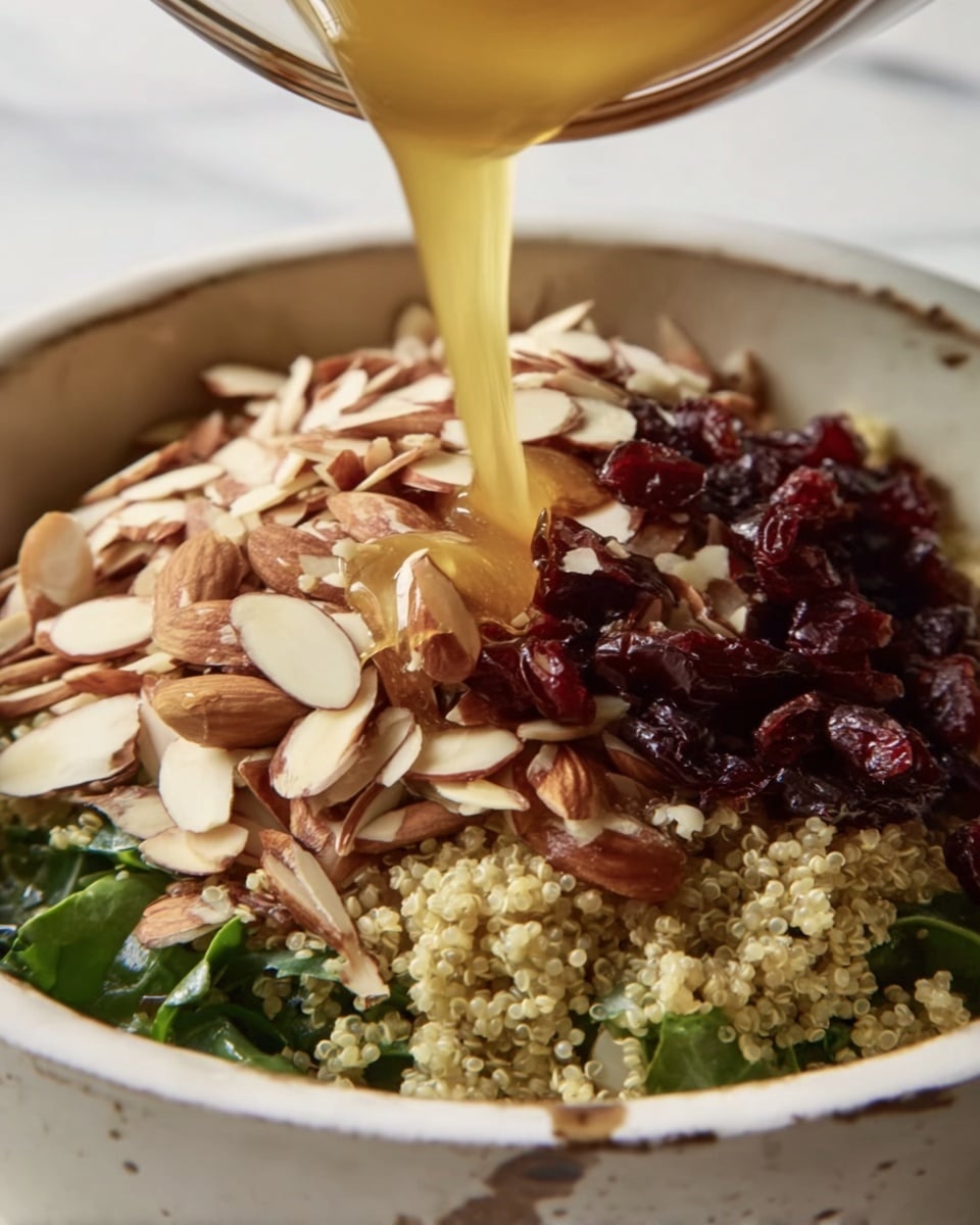 The image shows a close-up of a bowl filled with several layers. At the bottom, there is a layer of green leafy vegetables, above it a layer of small, light-colored grains, likely quinoa. On top of the grains, there is a thick layer of sliced almonds, light beige with brown edges. Mixed with the almonds are small, dark red dried berries. A thin stream of golden honey is being poured over the top, shining and flowing over the nuts and berries. The bowl is white with a slightly worn texture and sits on a white marbled surface. photo taken with an iphone --ar 4:5 --v 7