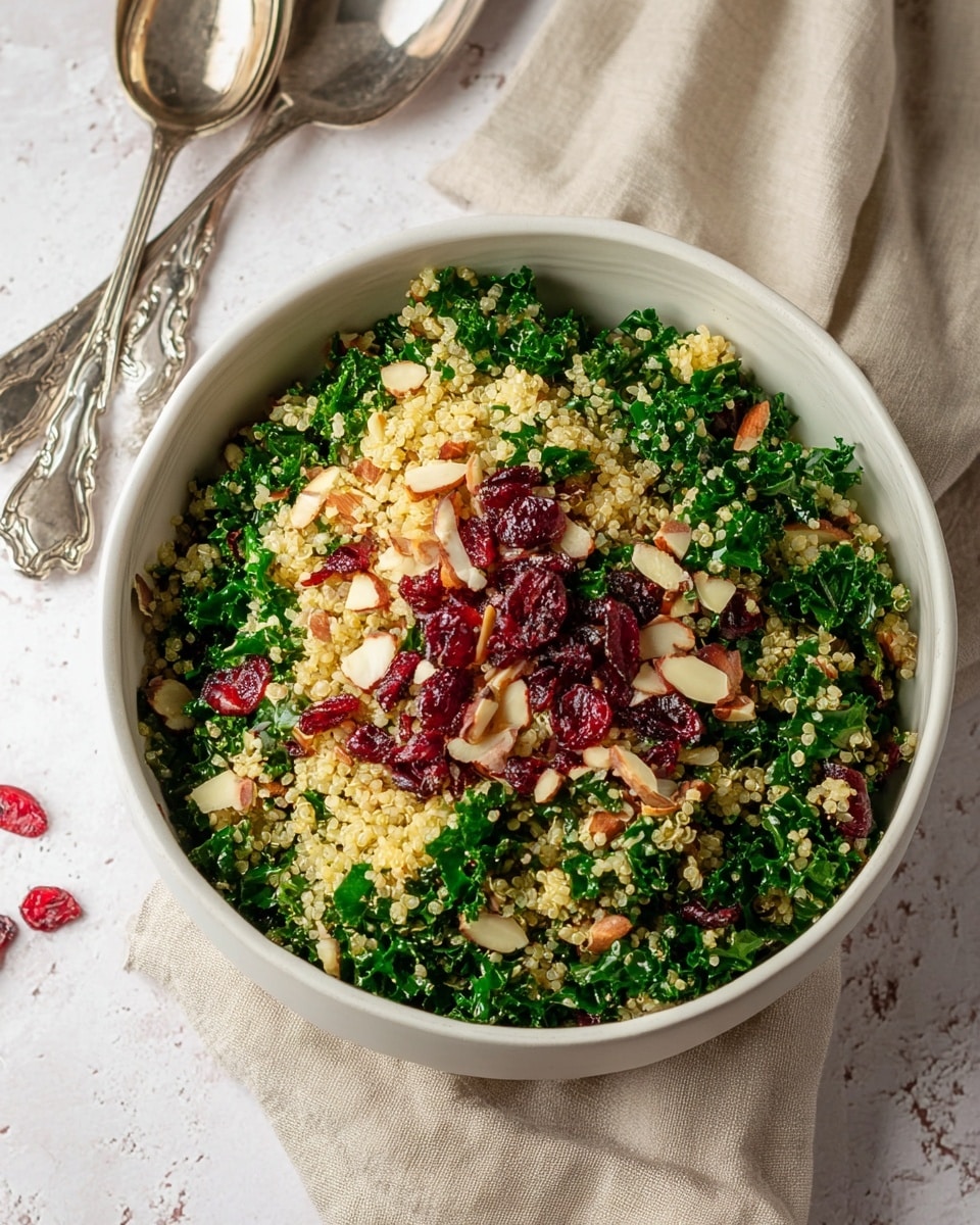 A white bowl filled with a salad showing three main layers: the base layer is light yellow quinoa grains with a fluffy texture; the middle layer consists of bright green curly kale leaves, chopped and mixed evenly throughout; the top layer is sprinkled with red dried cranberries and pale beige almond slices scattered on the surface. The bowl is placed on a white marbled texture with a beige cloth nearby and two vintage silver serving spoons beside it, shiny and ornate. photo taken with an iphone --ar 4:5 --v 7