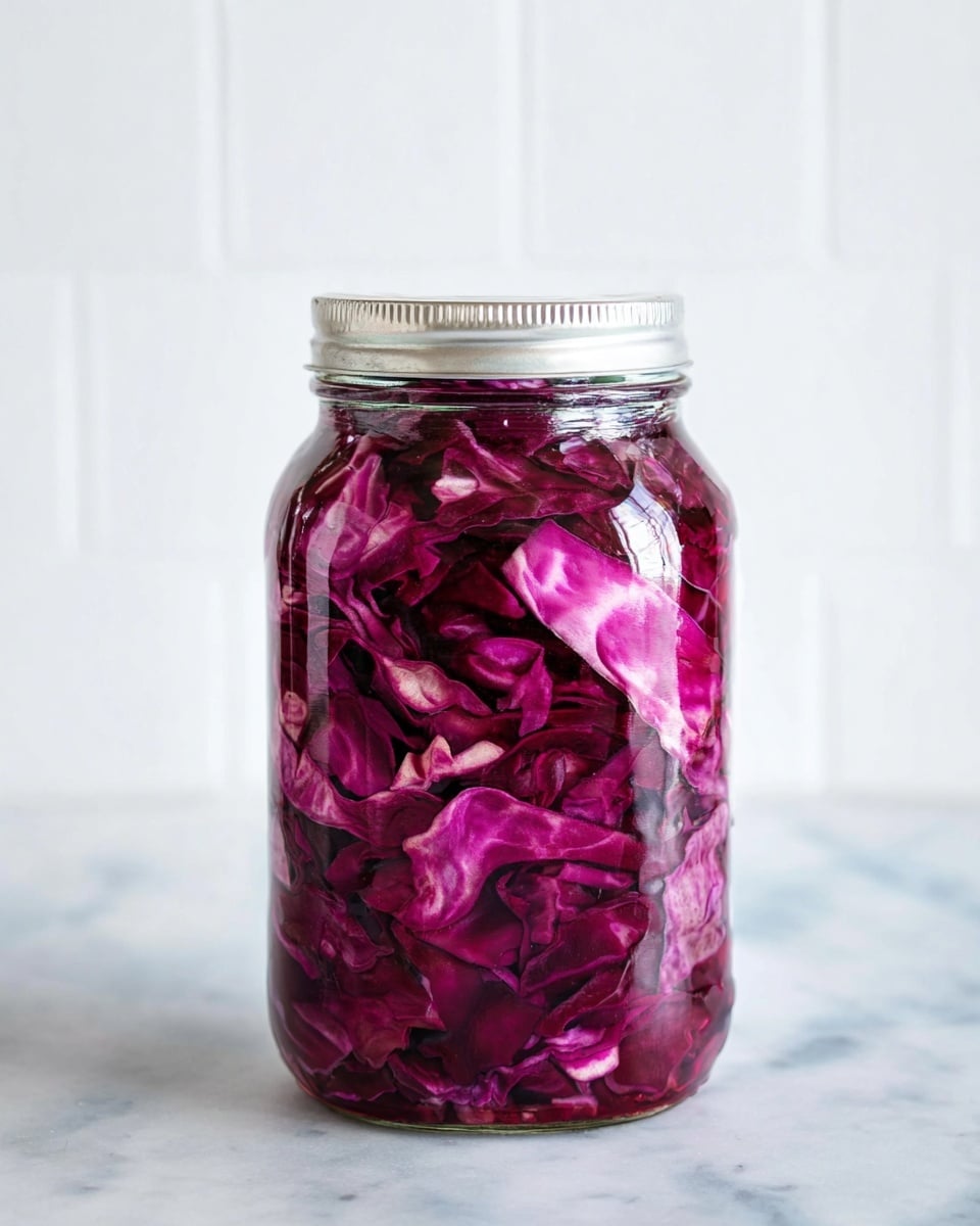 A clear glass jar filled with chopped red cabbage leaves, showing layers of deep purple and lighter pinkish edges soaked in liquid. The jar is full to the top with tightly packed cabbage pieces, some slightly curled. The jar sits on a white marbled surface with a plain white tiled background. Photo taken with an iphone --ar 4:5 --v 7