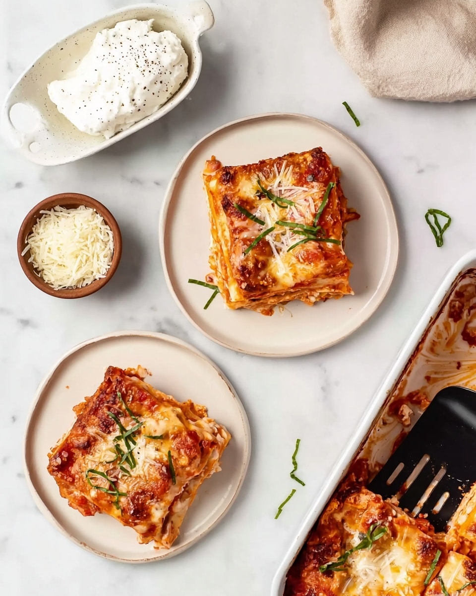 The image shows two square pieces of baked layered food on white round plates placed on a white marbled surface. Each piece has layers of creamy sauce, tomato sauce with visible chunks, and melted cheese on top with some green herb strips sprinkled over. There is a white dish with a scoop of white creamy sauce with black specks in the top left corner. Nearby, a small brown bowl holds a finely grated white cheese. A white rectangular baking dish containing more of the baked dish is in the upper right, with some pieces missing and a black slotted spatula resting inside. Small green herb strips are scattered around the plates and dishes. photo taken with an iphone --ar 4:5 --v 7