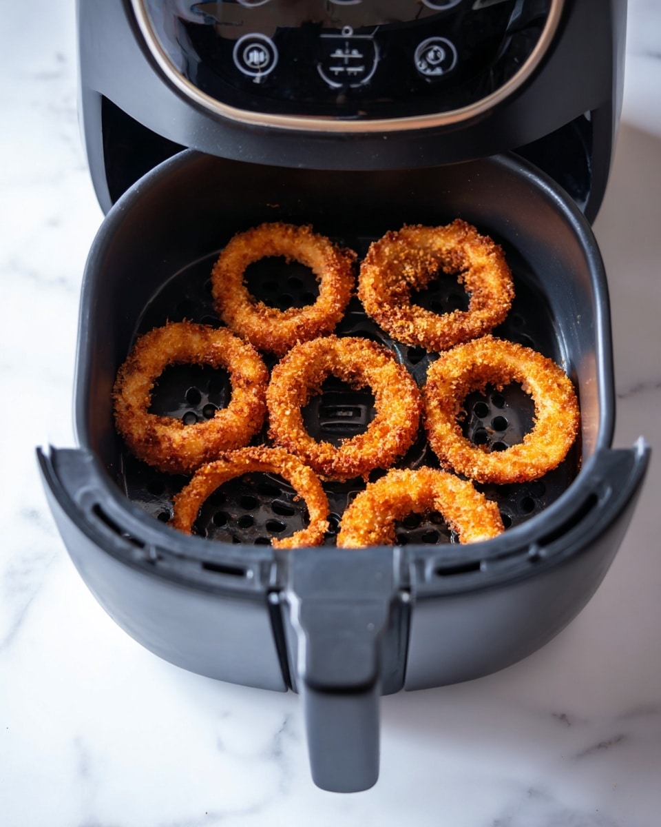Inside a black air fryer basket, there are seven golden brown onion rings arranged loosely in a single layer, showing a crunchy texture with some darker browned spots on their crispy coating. The air fryer is open, with its black inner tray visible beneath the onion rings, and the electronic control panel above showing a timer and buttons. The scene has a clean white marbled surface beneath, and a woman's hand holds the handle of the air fryer drawer. Photo taken with an iphone --ar 4:5 --v 7
