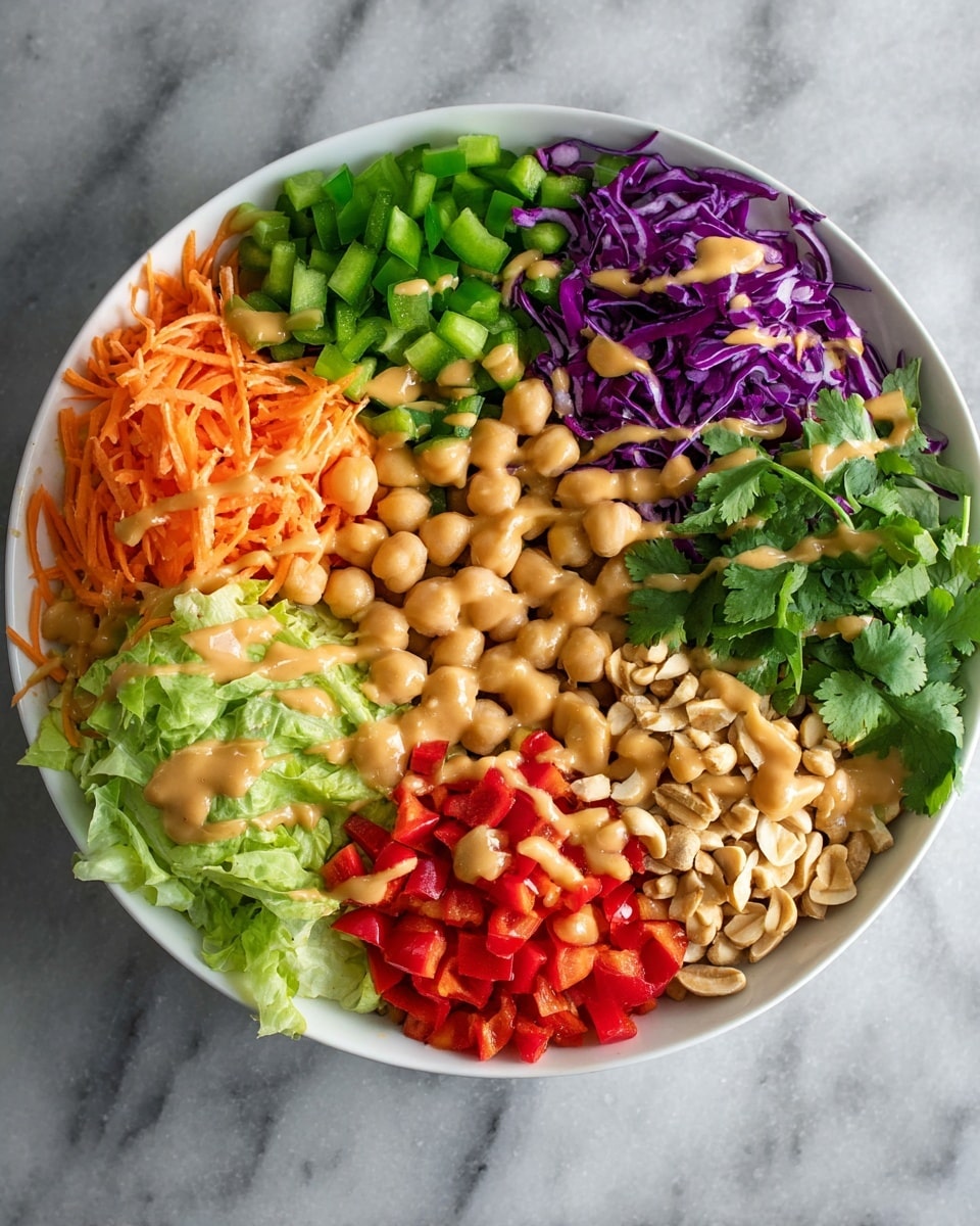 A top view of a white bowl filled with seven separate layers of food arranged in a circle: finely shredded orange carrots at the top left, chopped green bell peppers next to it, finely chopped purple cabbage at the top right, chopped light green lettuce on the right, a pile of beige chickpeas with a creamy light brown sauce drizzled on top near the bottom right, roasted peanuts with the same sauce nearby, diced red bell peppers, and chopped green onions just above them; some fresh cilantro leaves rest beside the green onions. The bowl sits on a white marbled surface. Photo taken with an iphone --ar 4:5 --v 7