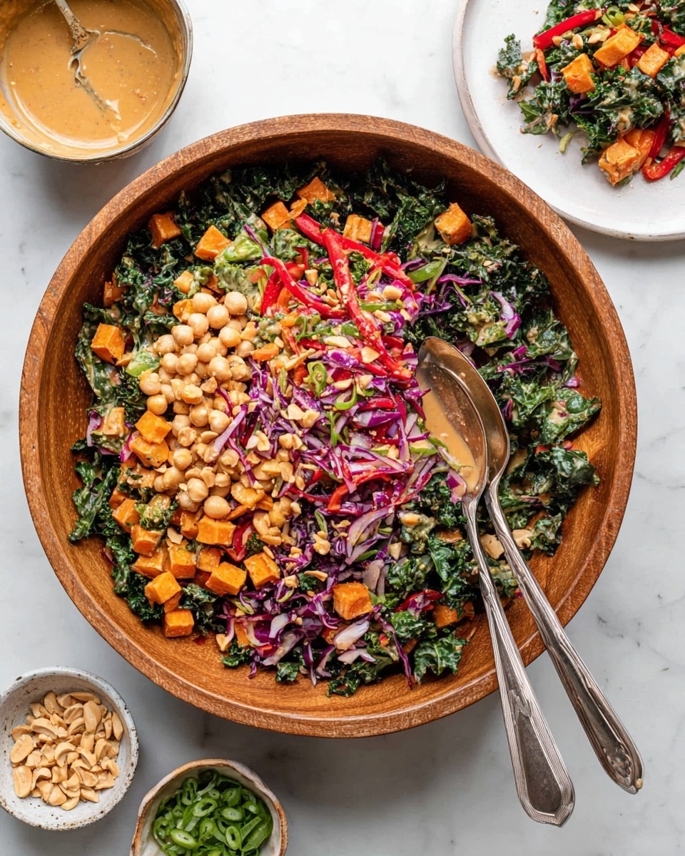 A large wooden bowl holds a colorful salad with five distinct layers: a base of dark green leafy kale, bright orange cubed sweet potatoes scattered throughout, light beige chickpeas spread evenly, thin red bell pepper strips, and shredded purple cabbage and green scallions mixed evenly. A creamy light brown dressing coats the salad lightly. Two silver serving spoons sit on the right side inside the bowl. Surrounding the bowl on a white marbled surface are three small dishes—one with a light brown peanut dressing with a spoon, one with chopped peanuts, and one with green scallions. A white plate in the upper right corner also holds a small portion of the same salad. Photo taken with an iphone --ar 4:5 --v 7