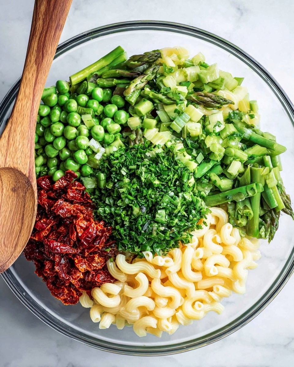 The image shows a clear glass bowl filled with five separate layers of ingredients. The bottom right section contains small elbow macaroni pasta in a pale cream color, smooth in texture. Directly above the pasta to the right is a bright green layer of finely chopped chives and parsley that look fresh and leafy. To the top left of the herbs is a layer of fresh green peas and asparagus pieces, showcasing different shades of green with a mix of round and slender shapes. Finally, on the bottom left, there is a layer of finely chopped sun-dried tomatoes with a deep red color and slightly rough texture. The bowl sits on a white marbled surface next to a light wooden spoon. Photo taken with an iphone --ar 4:5 --v 7