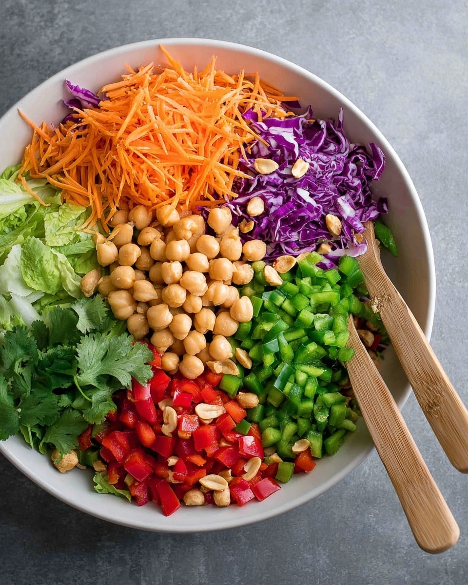 A white bowl filled with seven sections of fresh ingredients arranged side by side: orange shredded carrots, finely chopped green bell peppers, shredded purple cabbage, chopped green lettuce, whole light beige chickpeas, roasted peanuts, and diced red bell peppers. There are also some green scallions and fresh cilantro leaves adding extra green color near the bottom left. Two wooden salad forks lie on the right side of the bowl on a gray surface. Photo taken with an iphone --ar 4:5 --v 7