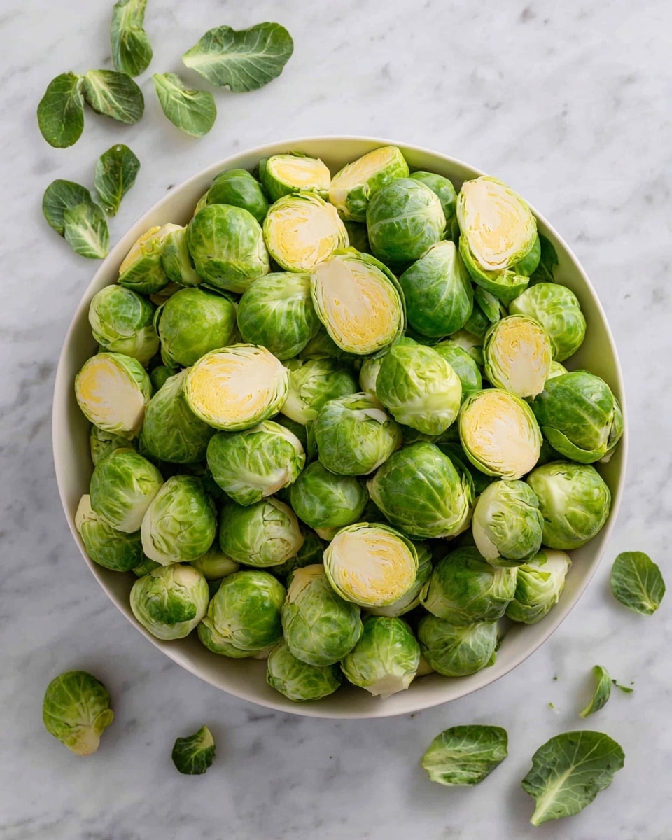 A white bowl filled with many halved Brussels sprouts, showing their round shape with light green outer leaves and pale yellowish centers, some loose green leaves scattered on a white marbled surface around the bowl photo taken with an iphone --ar 4:5 --v 7