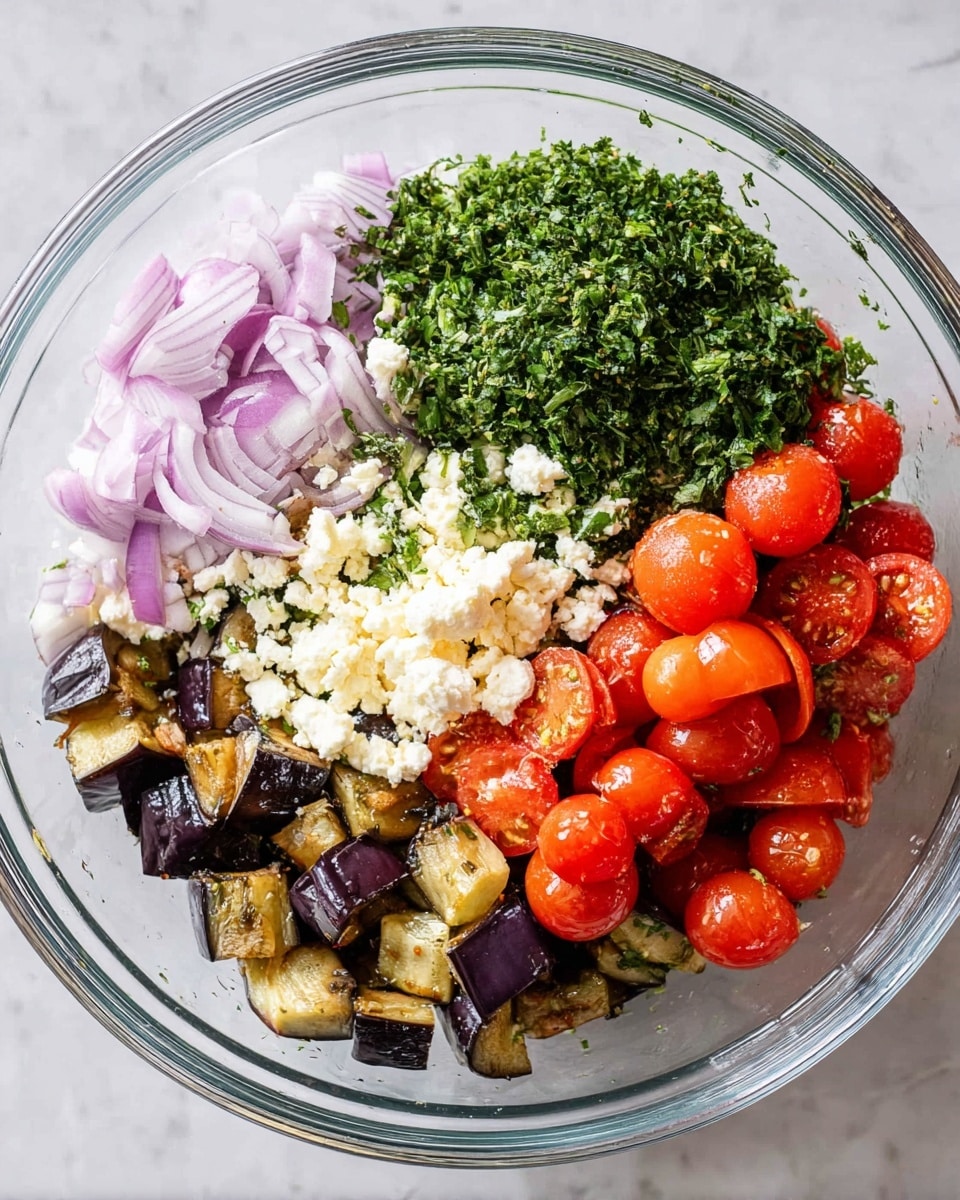 A clear glass bowl sits on a white marbled surface and holds a colorful mix of ingredients. The bottom layer contains small diced roasted eggplants showing dark purple skin and soft golden insides. Thin slices of red onion with a pale purple hue scatter over the eggplants. A big cluster of bright red cherry tomatoes, some whole and some sliced in half, cover one side of the bowl. Crumbled white cheese forms a soft and grainy pile next to the tomatoes. On the opposite side, fresh chopped herbs create a dense green mound with varying shades of light to dark green. The scene is lit brightly, showing clear textures and colors. Photo taken with an iphone --ar 4:5 --v 7