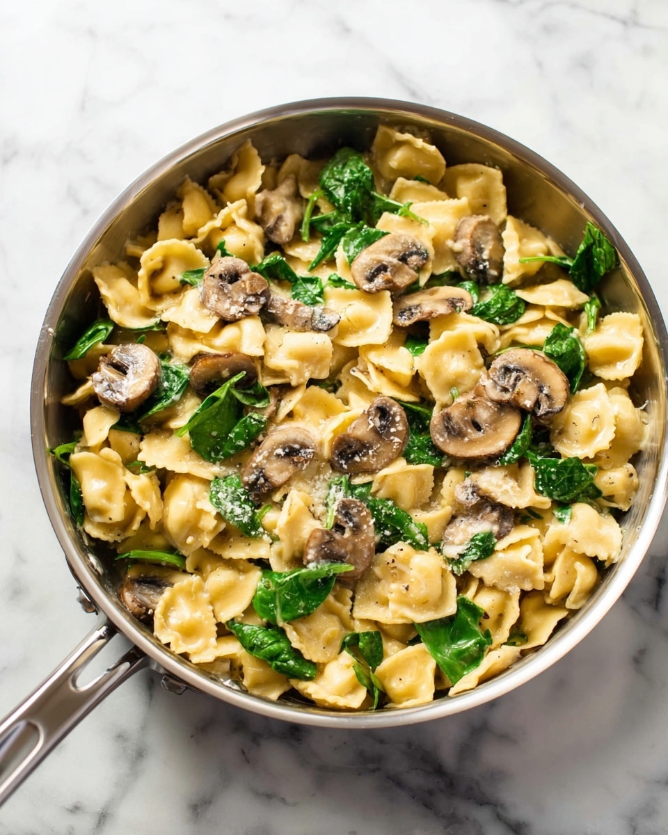 The image shows a silver pan filled with three layers of food on a white marbled surface. The base layer is small yellow pasta pieces shaped like rounded squares with ruffled edges. Scattered throughout, there are evenly mixed slices of light brown mushrooms and bright green spinach leaves. The pasta appears soft, coated in a creamy light sauce that blends well with the soggy texture of the mushrooms and fresh spinach. The pan has a shiny handle extending towards the front left. Photo taken with an iphone --ar 4:5 --v 7