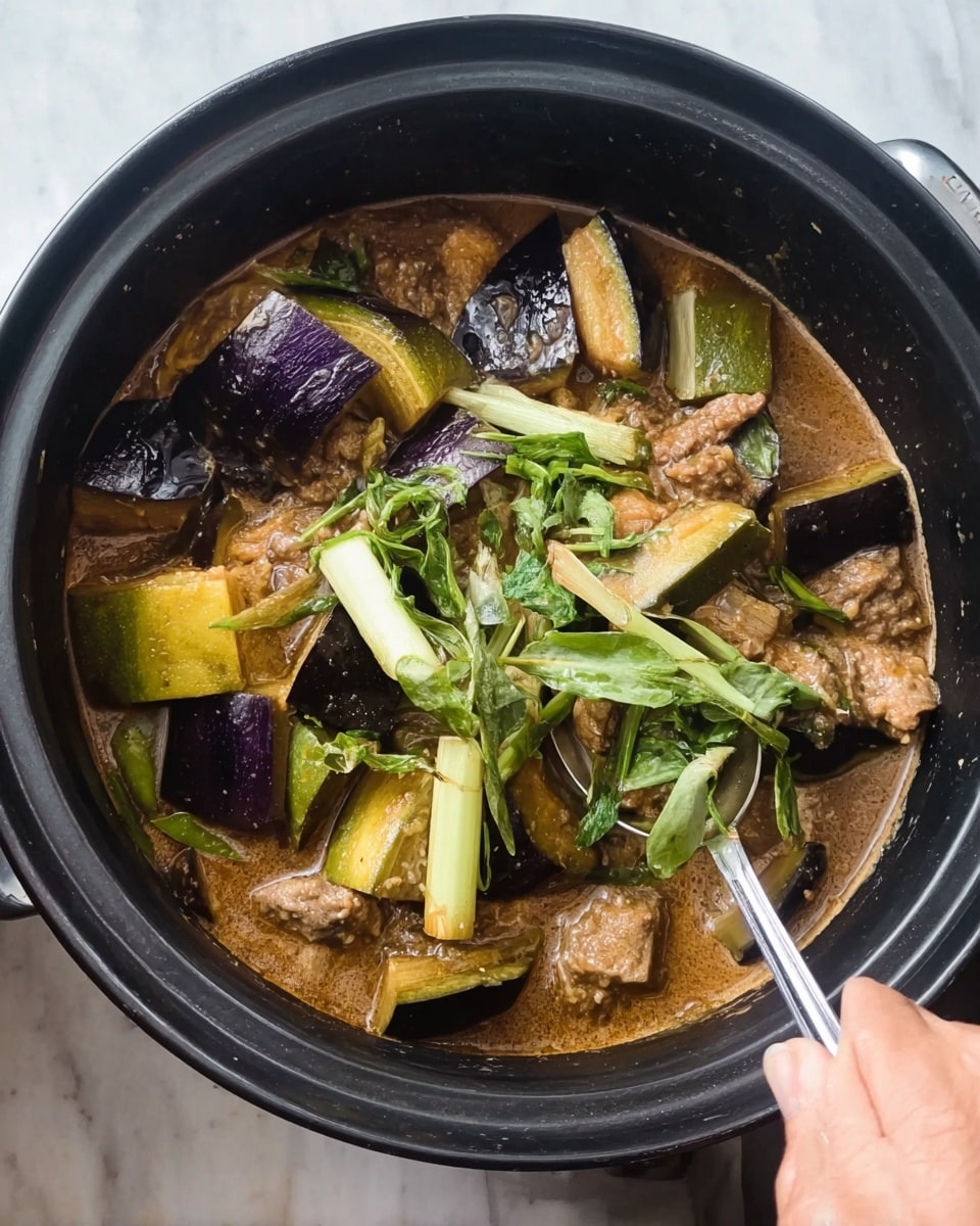 The image shows a black cooking pot filled with a stew-like dish. The dish contains several layers of cut eggplants, both greenish-yellow and deep purple, scattered throughout the pot. There are light brown, chunky pieces of meat mixed in with the eggplants, partly submerged in a thick, brown sauce. Bright green leafy vegetables and some long white vegetable pieces are spread on top, adding freshness. A silver spoon is held by a woman's hand, stirring the dish gently from the right side. The pot sits on a white marbled surface. photo taken with an iphone --ar 4:5 --v 7