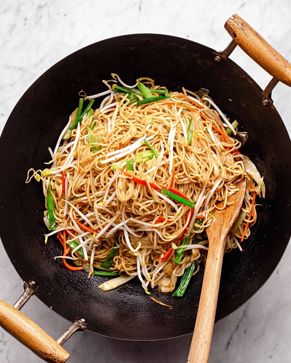 A black wok with light brown wooden handles and a wooden spatula is filled with stir-fried noodles and vegetables. The noodles are light golden brown and tangled together in the center, resting on a bed of fresh, white bean sprouts scattered throughout. Bright green onion stalks and thin, long orange carrot strips are mixed in evenly among the noodles and bean sprouts. The background features a white marbled surface. Photo taken with an iphone --ar 4:5 --v 7