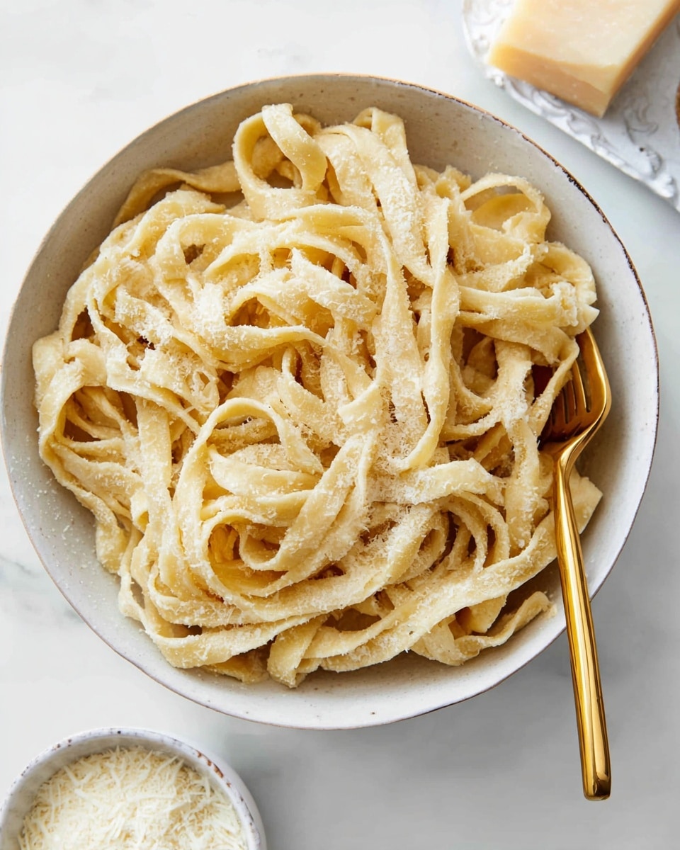 A white bowl filled with wide, thick noodles that have a pale yellow color and a slightly rough texture sprinkled with grated cheese. A gold fork is twirling some noodles near the center of the bowl. To the lower left of the bowl, there is a small white bowl with extra grated cheese. The entire scene is set on a white marbled surface with a white dish holding a block of cheese visible in the upper right corner. photo taken with an iphone --ar 4:5 --v 7